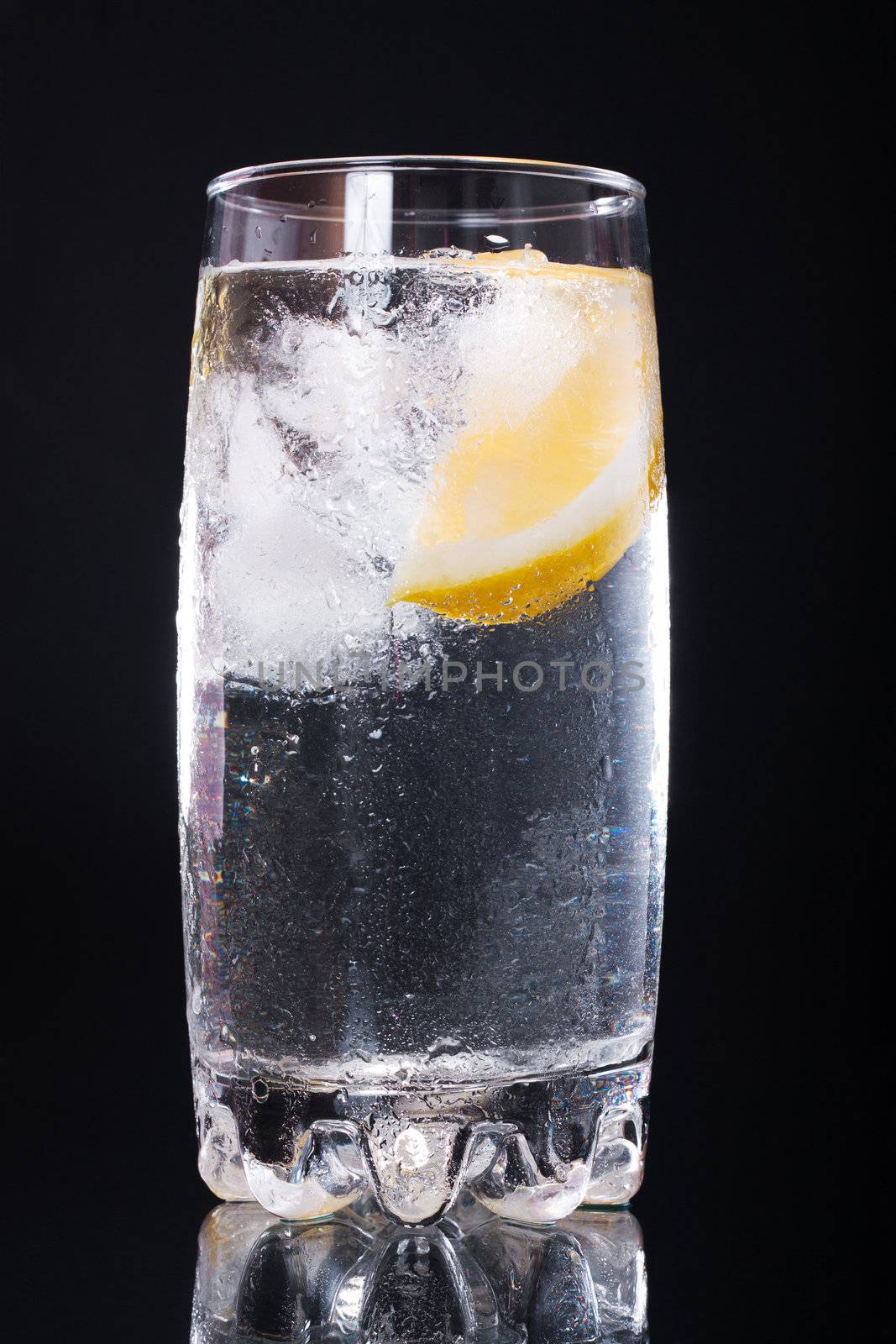 Mineral water with ice and lemon in a glass on a black background