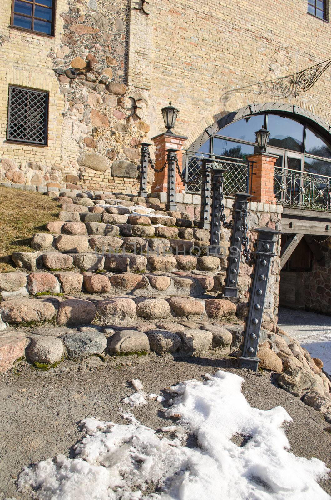 stone cobbly staircase with steel railings and light lamp leading to retro manor and snow remain in spring.
