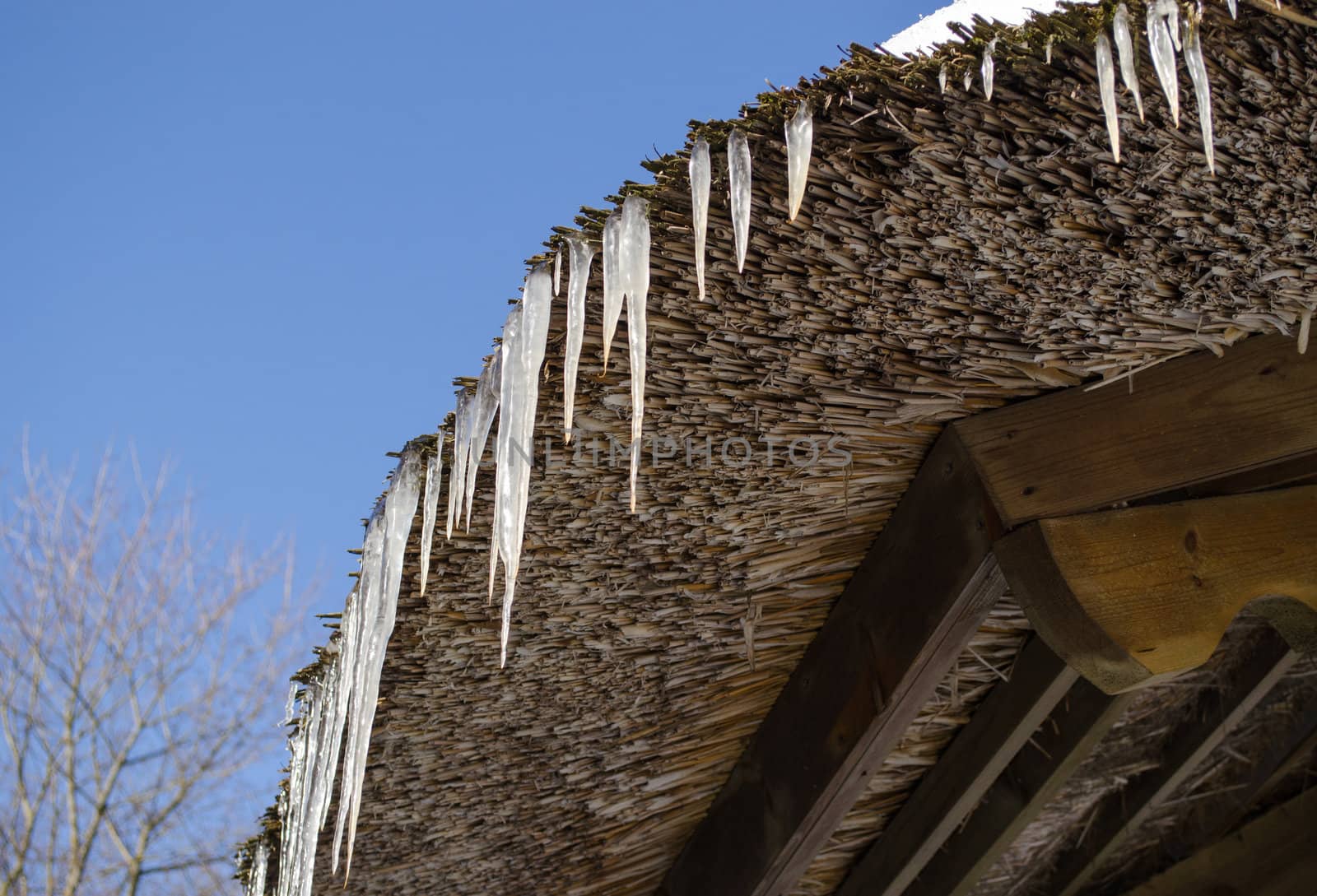 small icicles on retro straw roof on background of dark blue sky in winter.