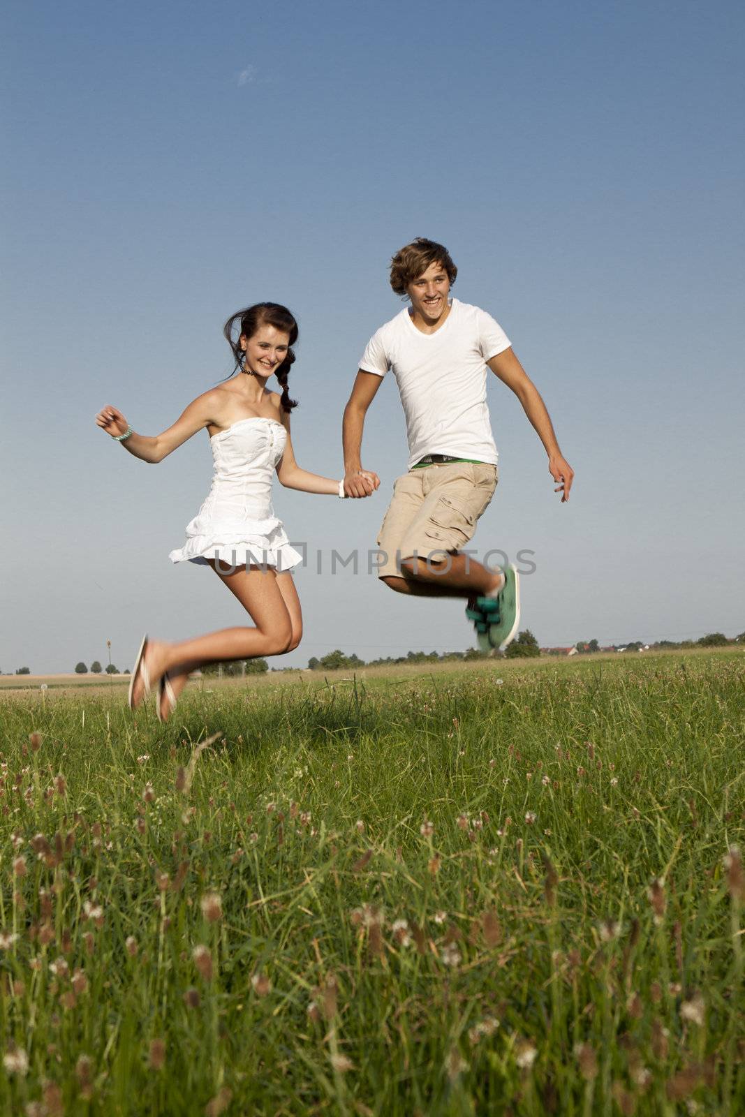 young happy couple jumping outside in summer on field 