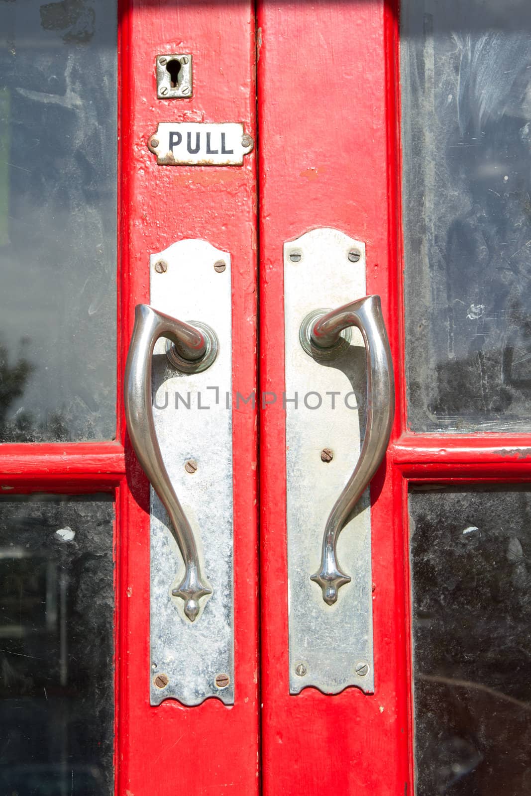 A red painted wooden door with a pair of metal retro doorhandles and a pull sign and keyhole.