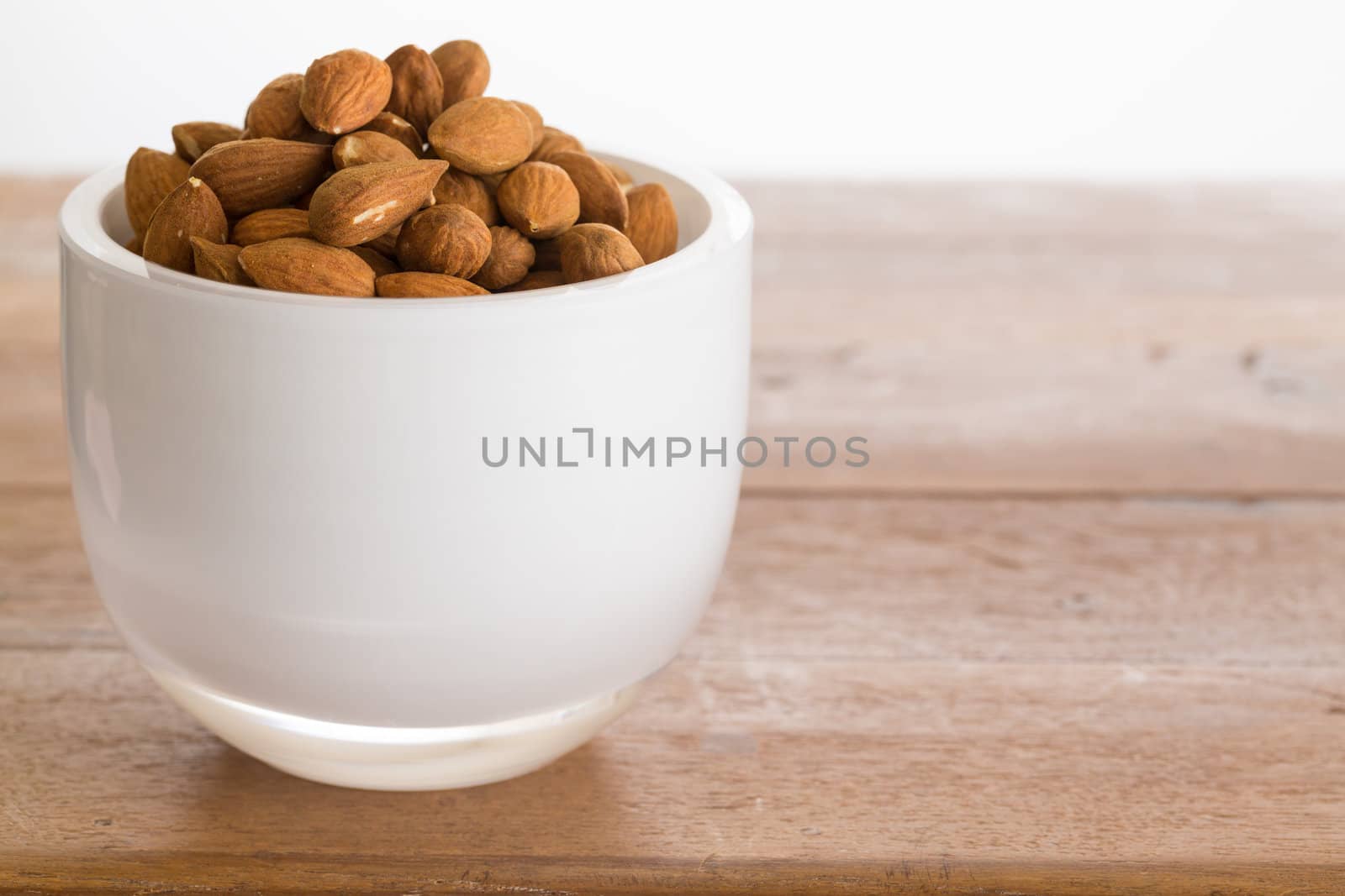 Raw almond nuts in white glass bowl on old wooden table
