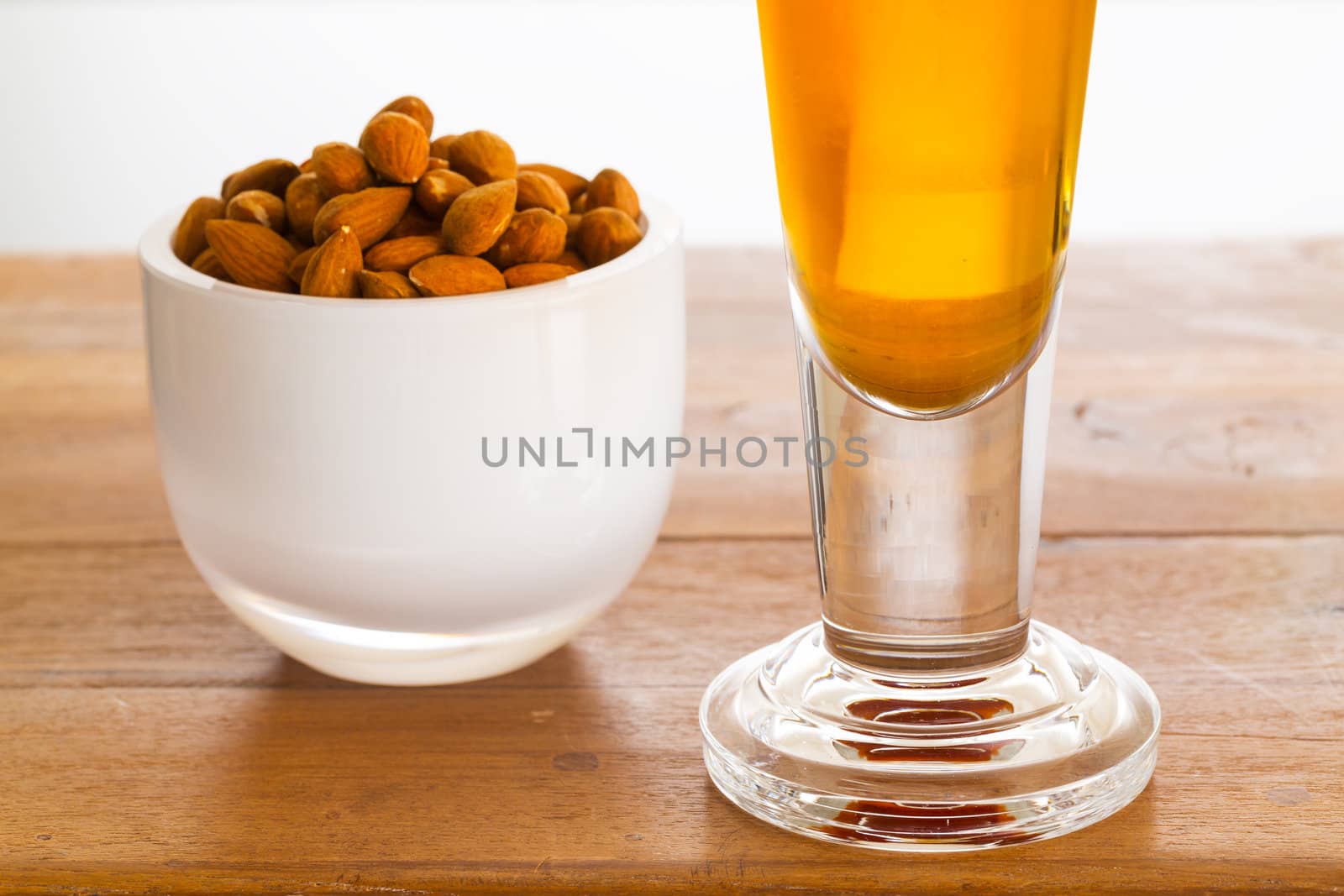 Raw almond nuts in white glass bowl on old wooden table with glass of cold beer