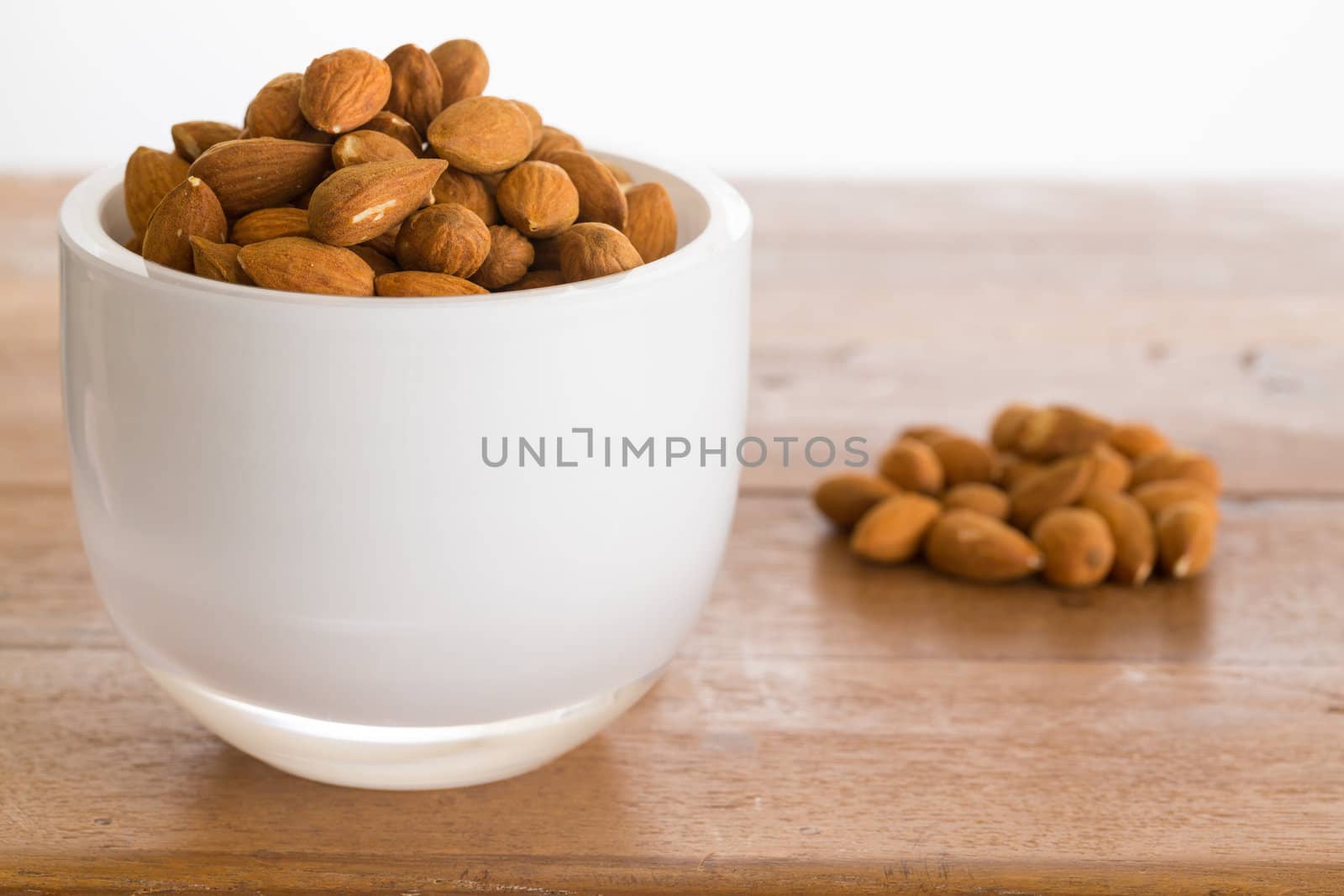 Raw almond nuts in white glass bowl on old wooden table