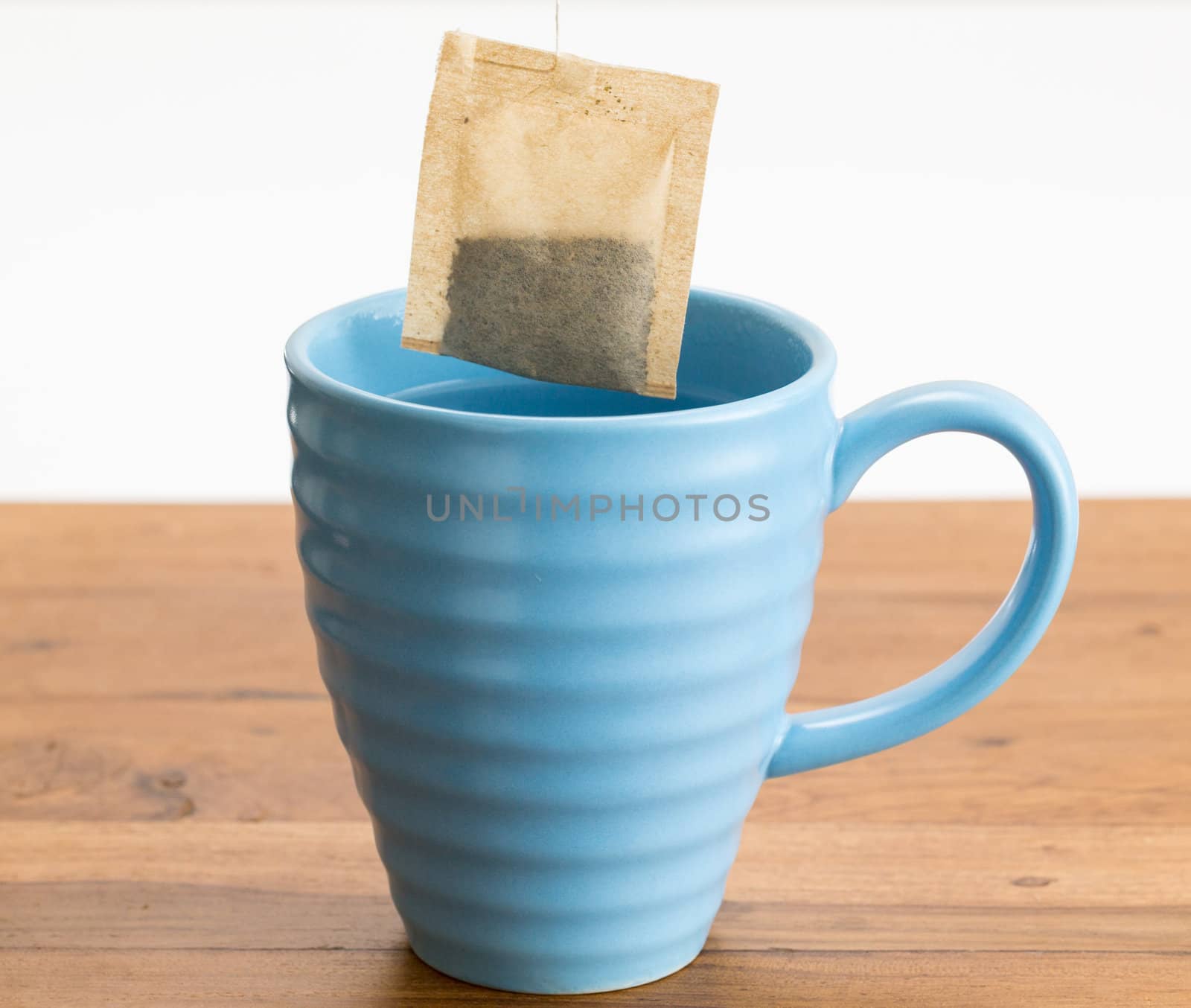 Organic green tea or herbal tea being lowered into a blue mug on wooden table