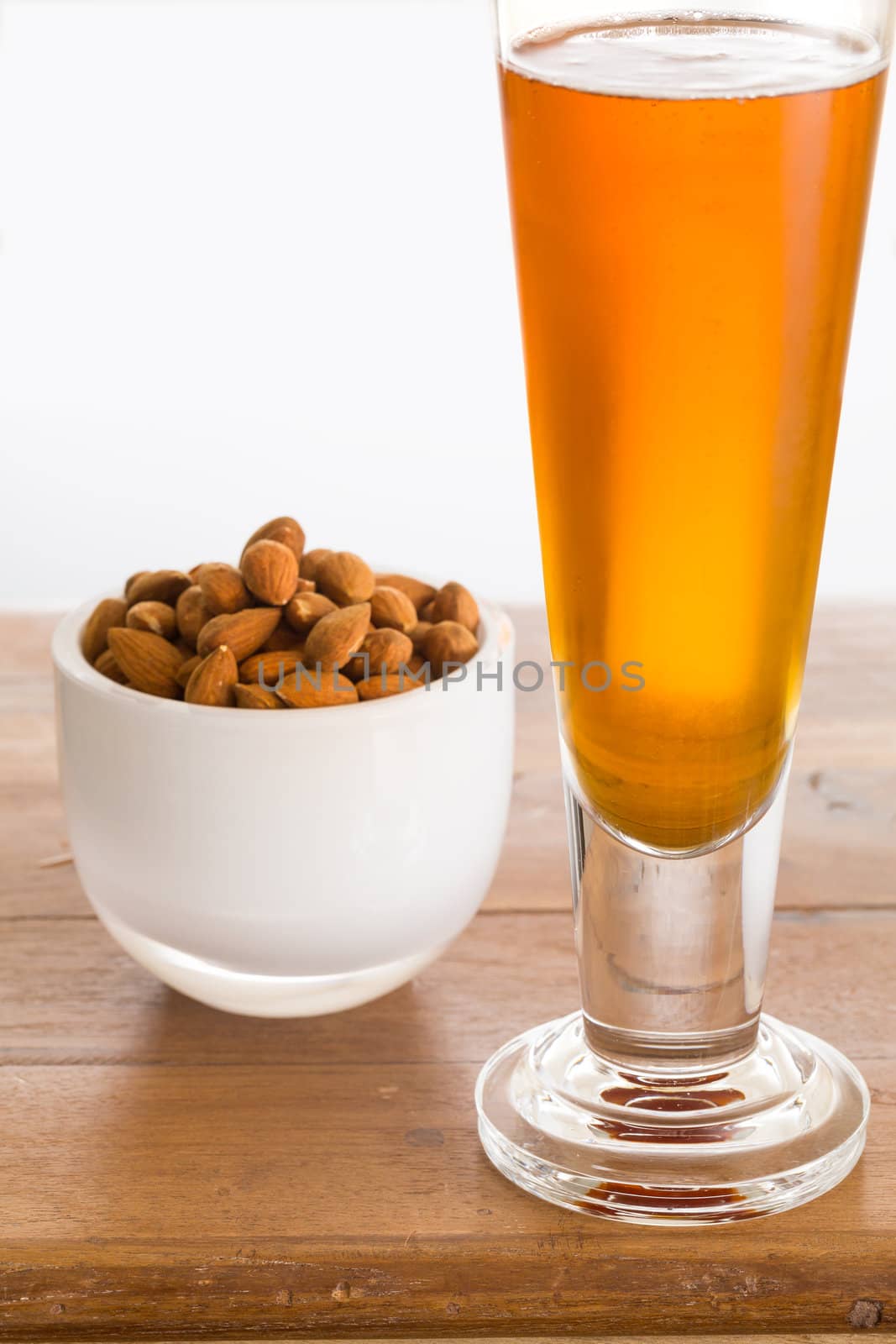 Raw almond nuts in white glass bowl on old wooden table with glass of cold beer