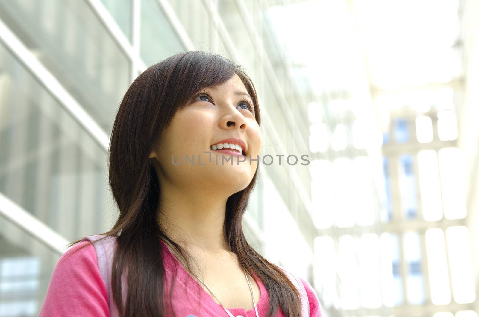 A young Asian girl looking far away to bright light in front of a modern building.