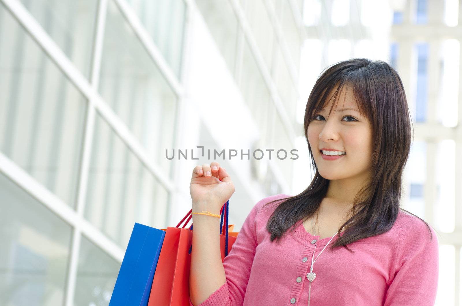 Beautiful young Asian girl holding paper bags, modern building as background