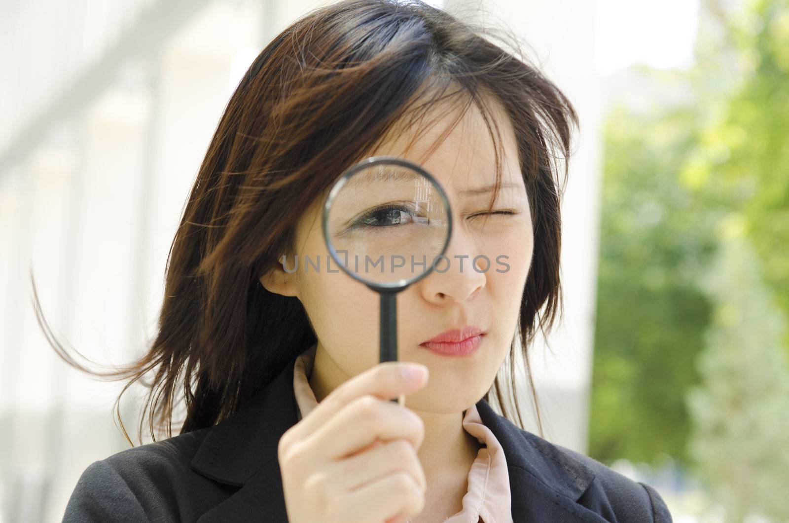 Asian business woman with magnifying glass to the eye