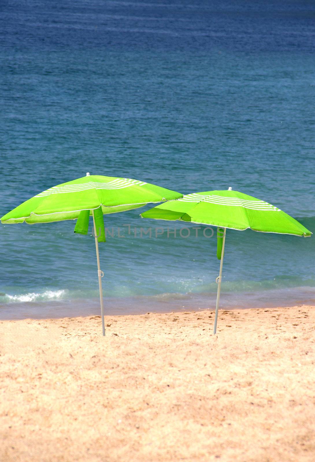 Two green sun umbrellas on the beach  by tanouchka