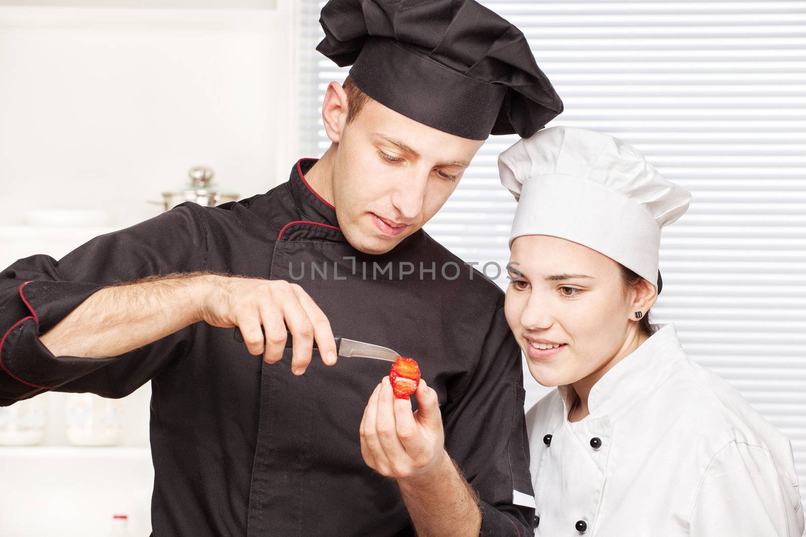 Senior chef teaches young chef to decorate strawberry