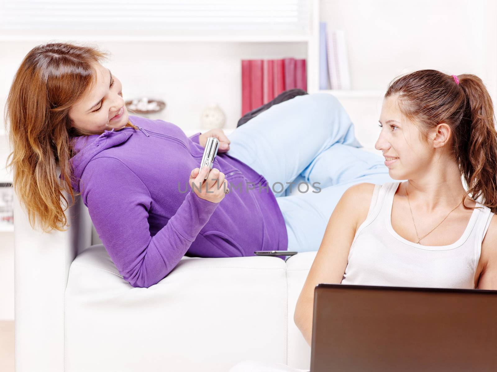 Two happy teenage girls having fun using electronic gadgets by imarin