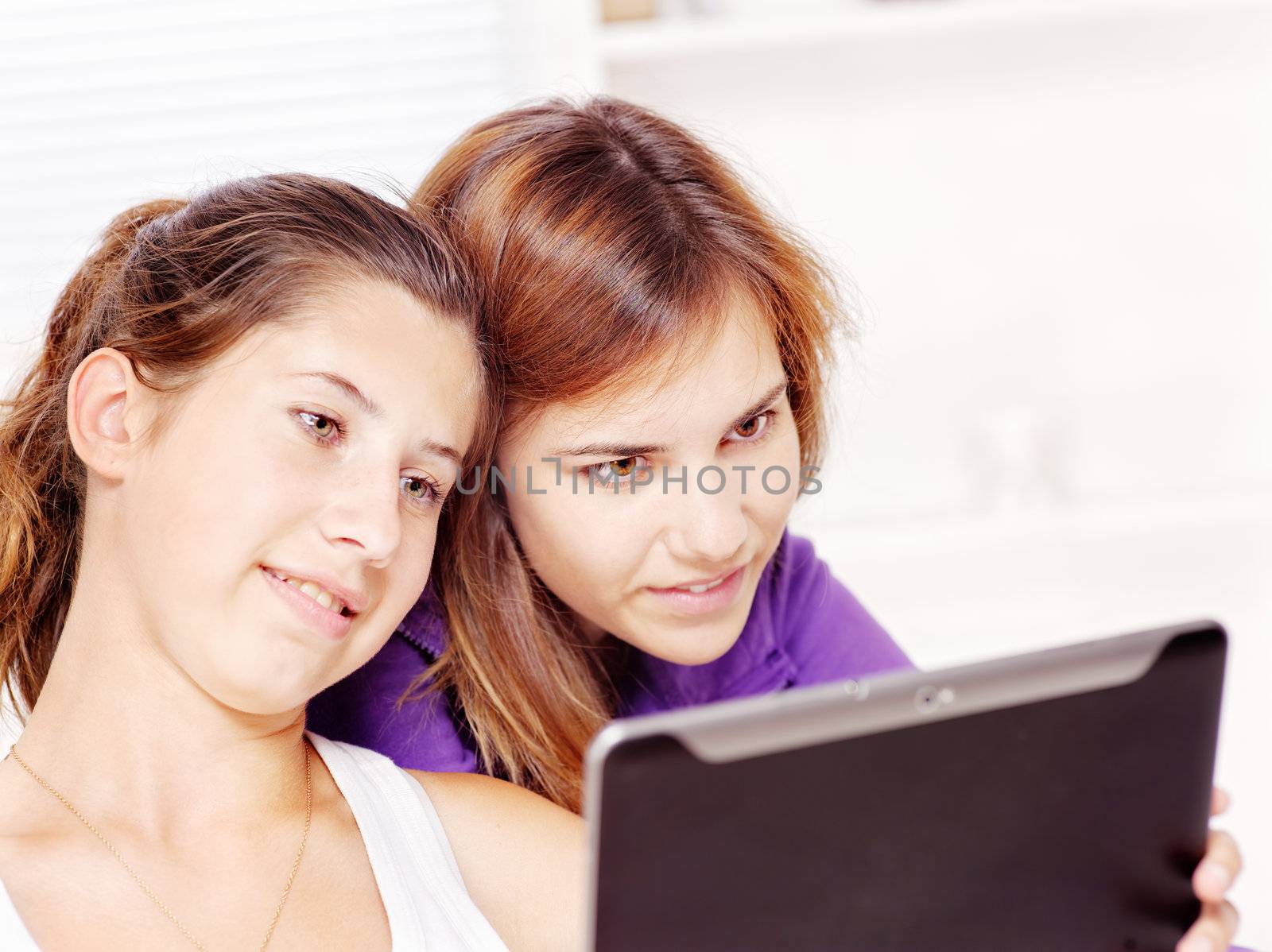 Two teenage girls using tablet computer at home
