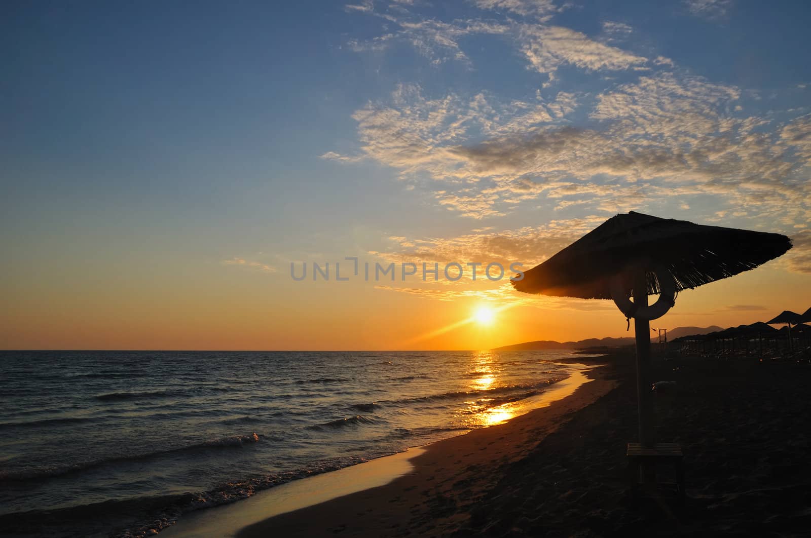 Umbrella on sandy sea beach at sunset stock photo