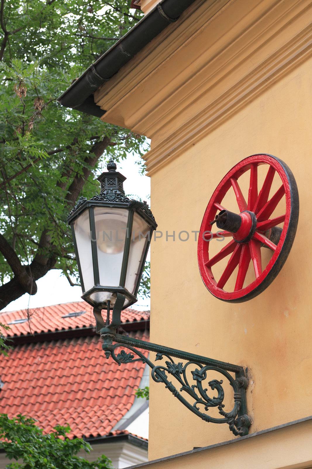 Stylish vintage lantern and red cart wheel on building wall