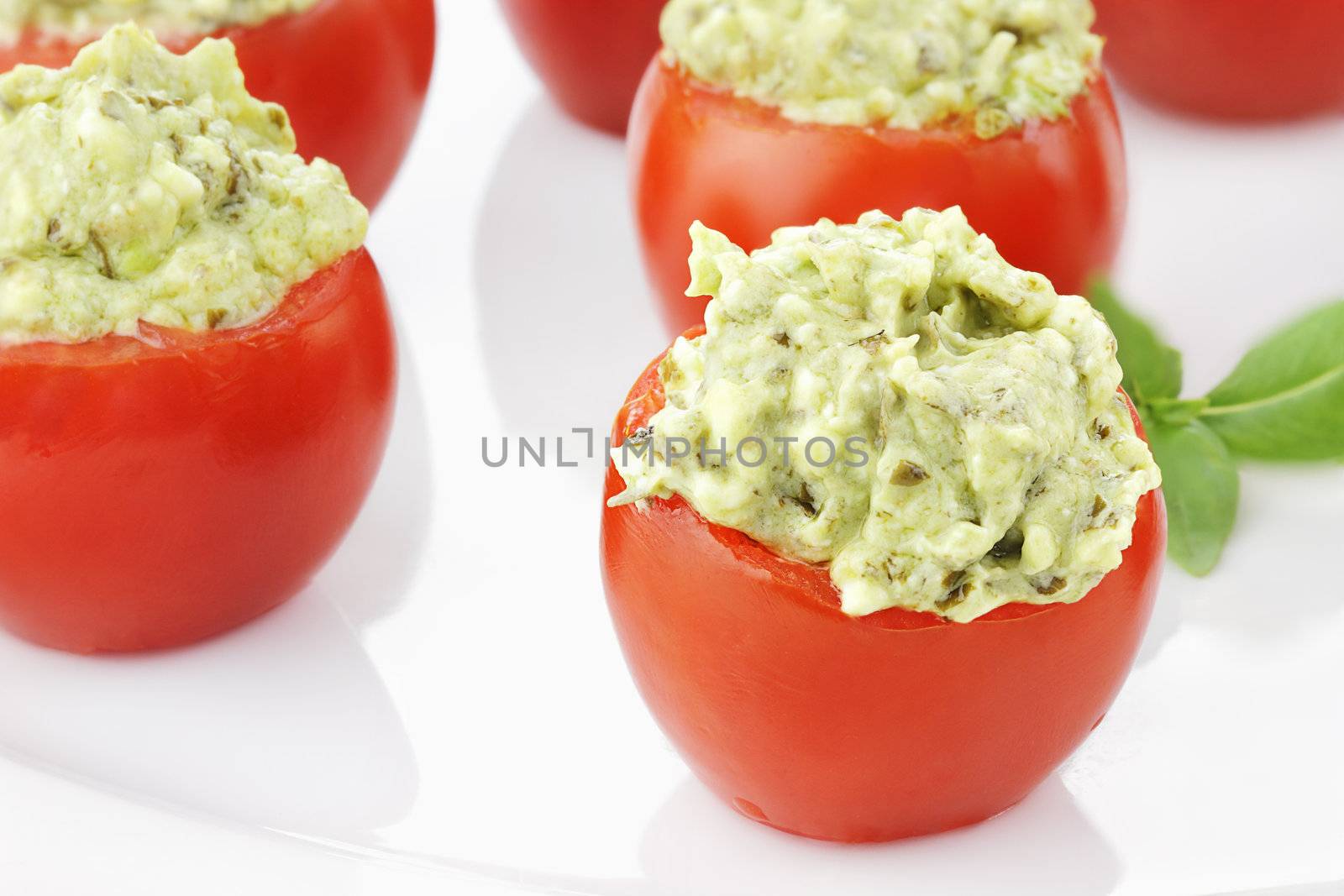 Stuffed Tomatoes filled with a pesto and avocado mixture. Extreme shallow depth of field with selective focus on tomato in foreground.