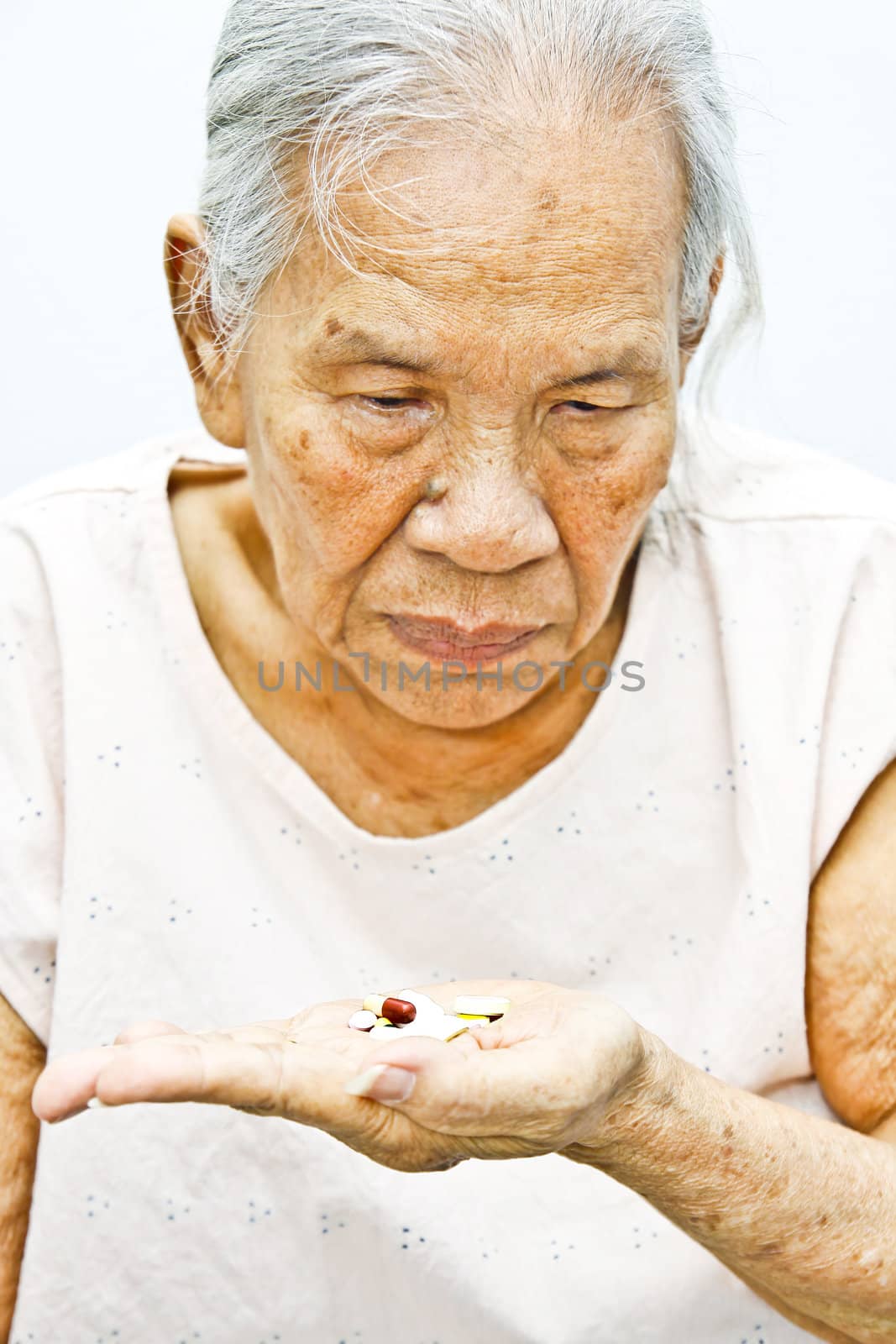 Old woman looking at pills in her hand.