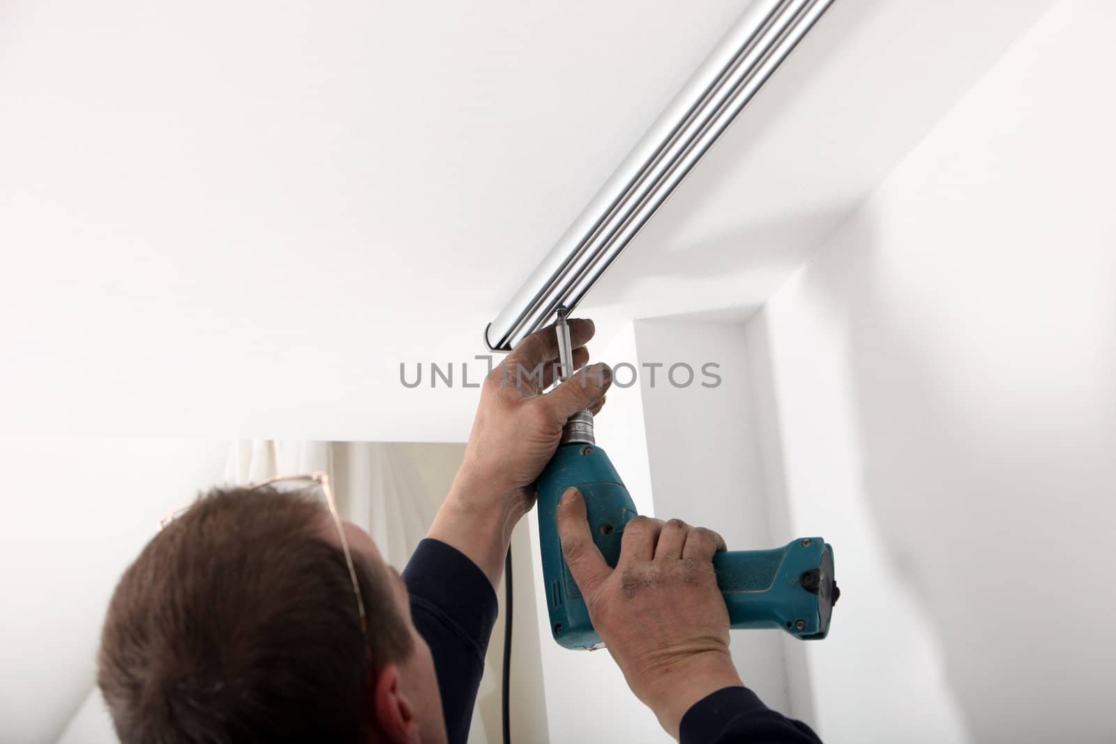 Tha arm of an artisan using a portable cordless drill to fit a length of aluminium curtain track to the ceiling