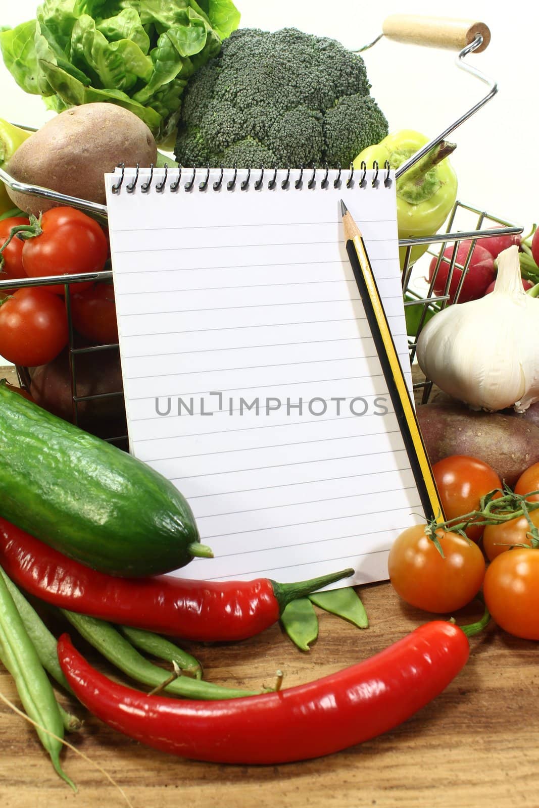 Basket with fresh vegetables, shopping list and pencil on a wooden background