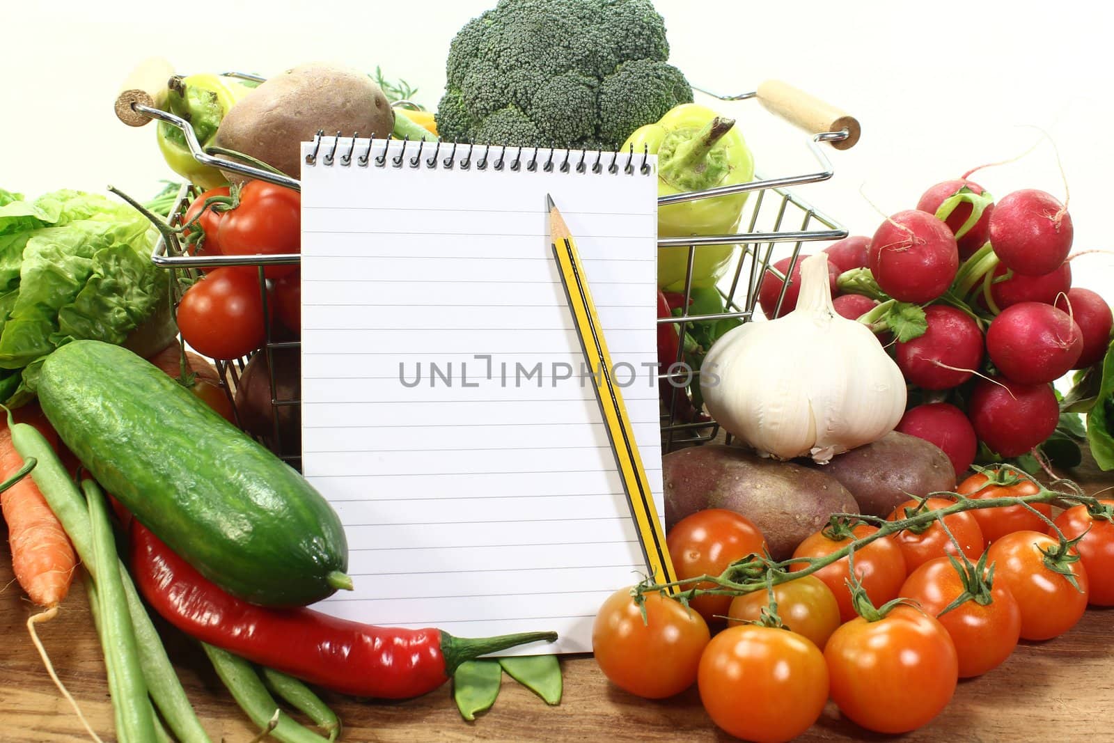Shopping list with basket, pencil and fresh vegetables on a wooden background