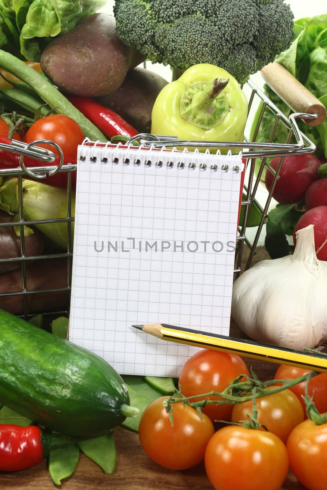 Basket with fresh vegetables and shopping list and pencil on a wooden background