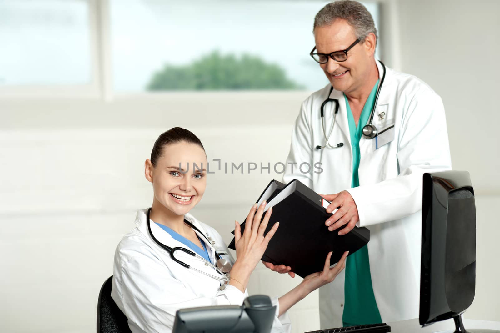 Male doctor handing over files to female doctor by stockyimages