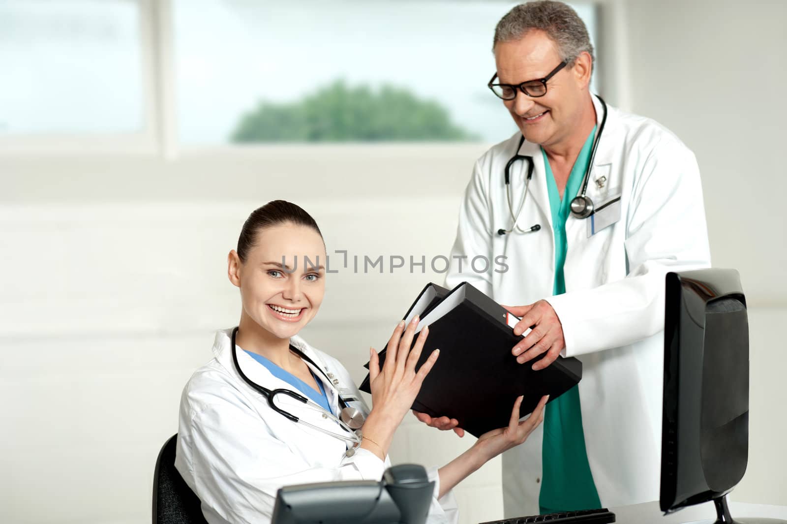 Male doctor handing over files to female doctor. Shot in lab