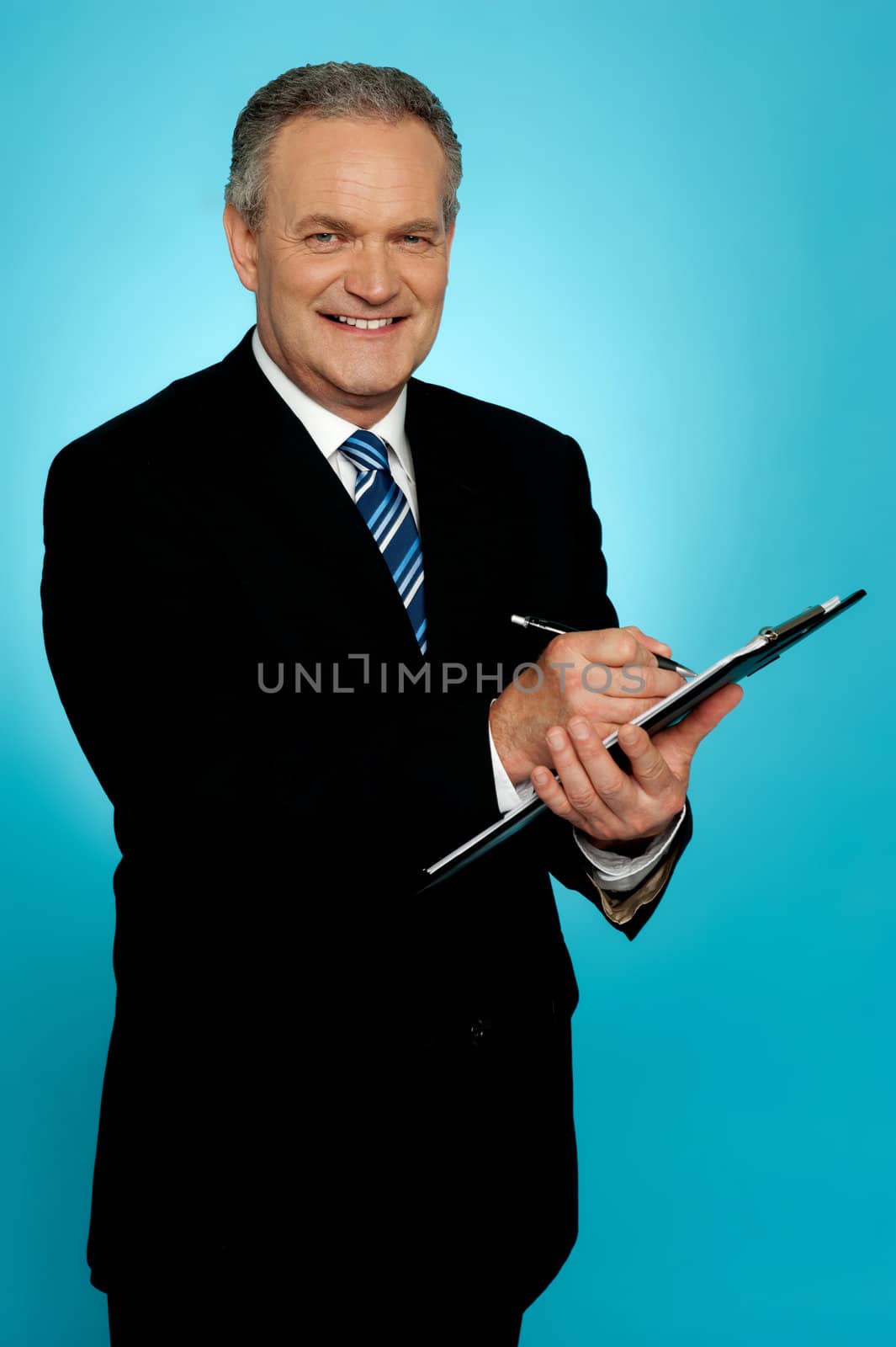 Smiling businessman writing on clipboard and looking at camera