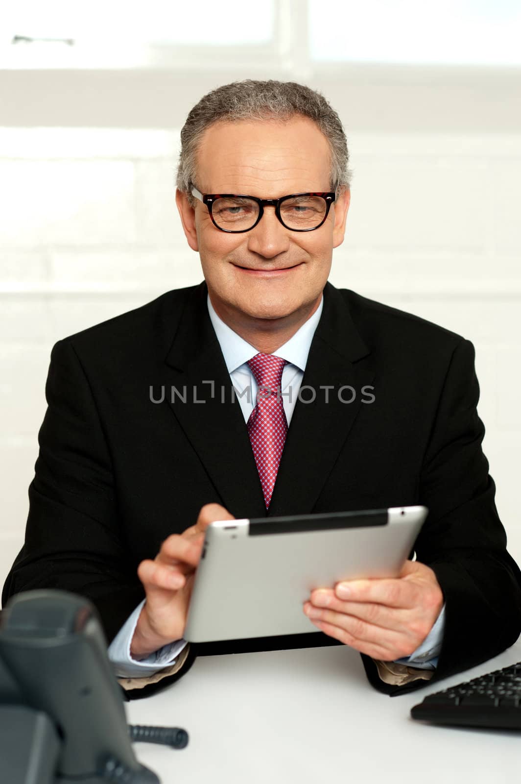 Senior executive sitting with tablet pc in hands and smiling at camera