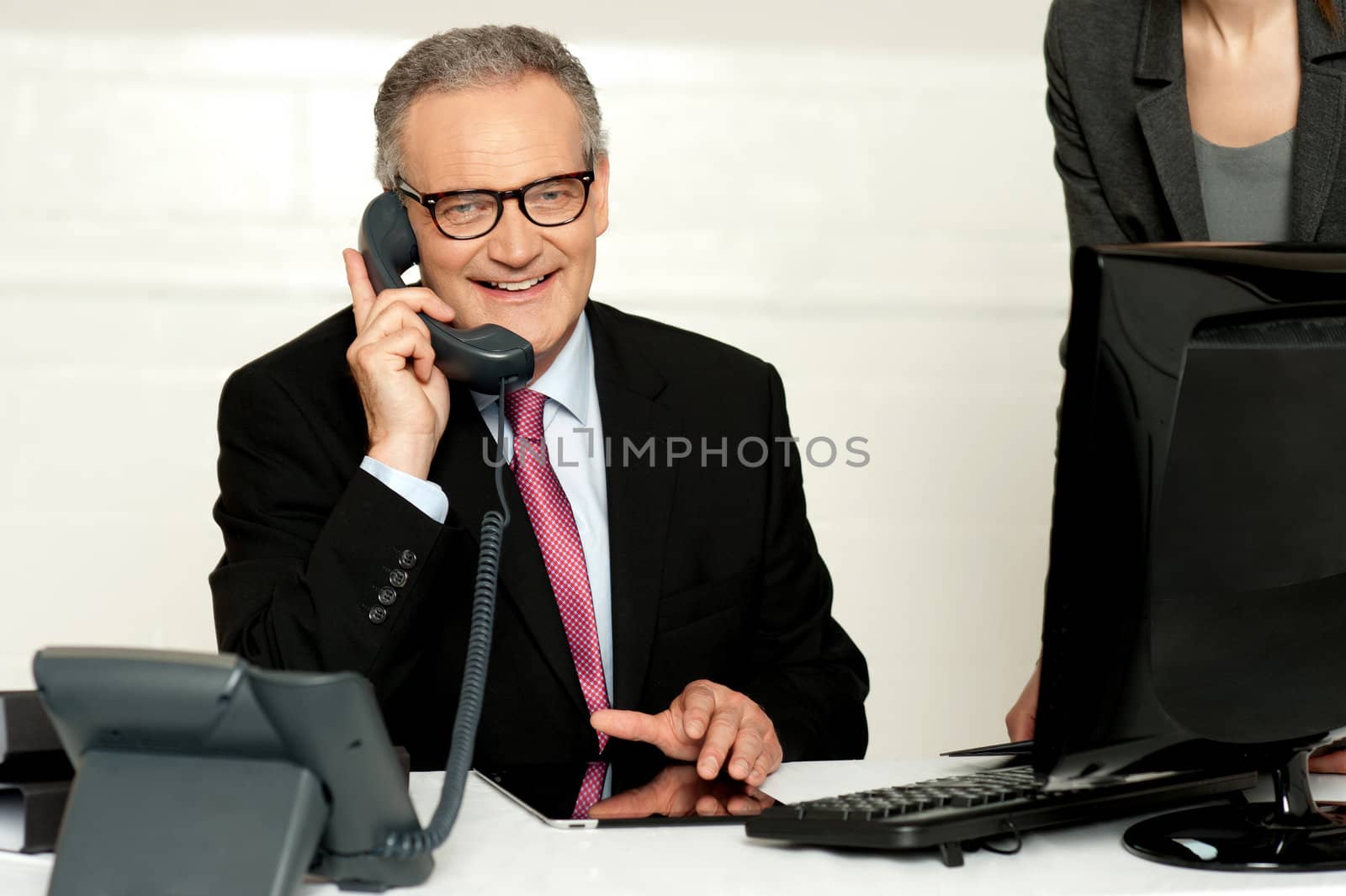 Aged businessman communicating on phone with secretary standing beside