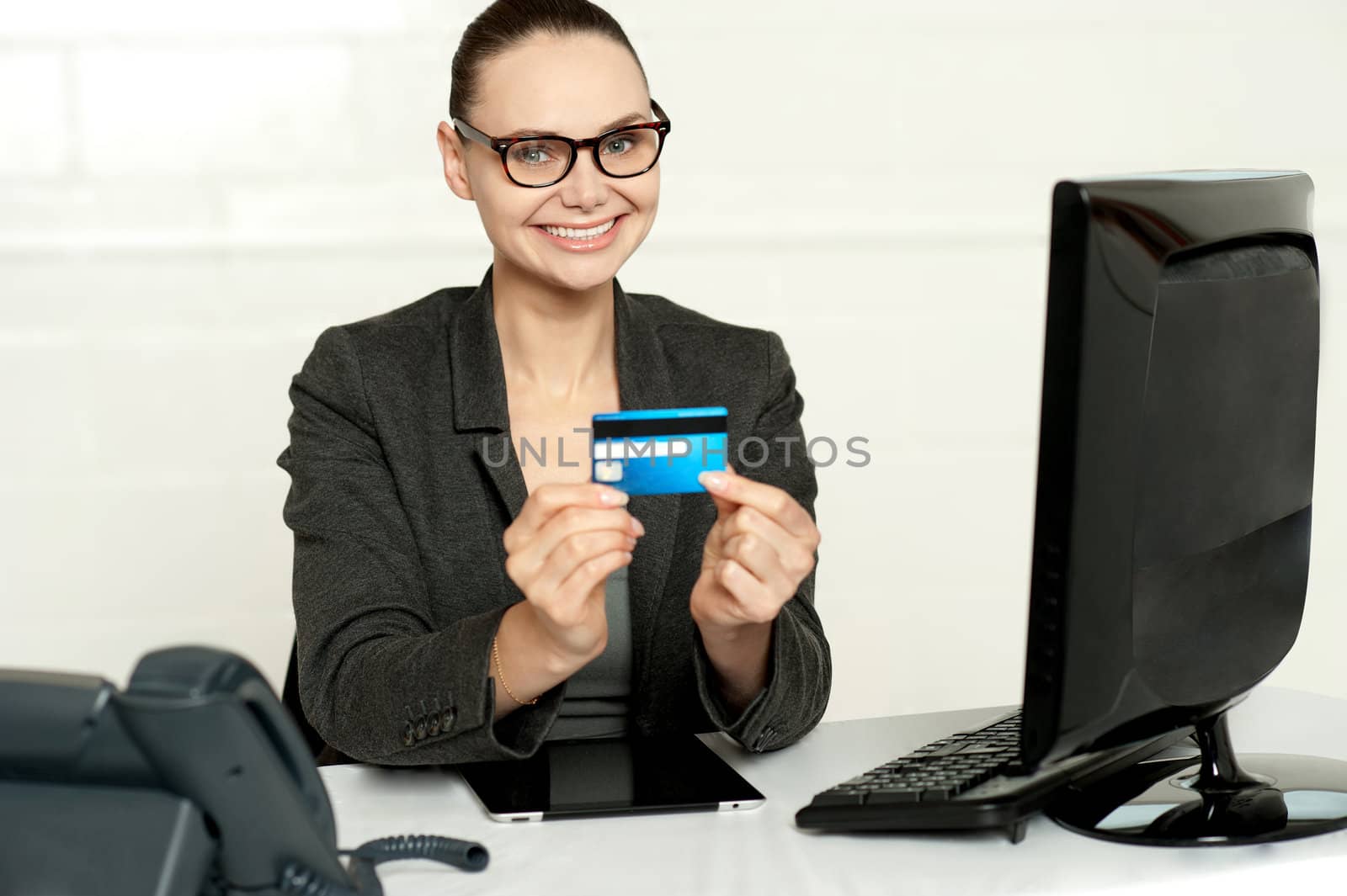 Smiling corporate lady in her office showing credit card to camera