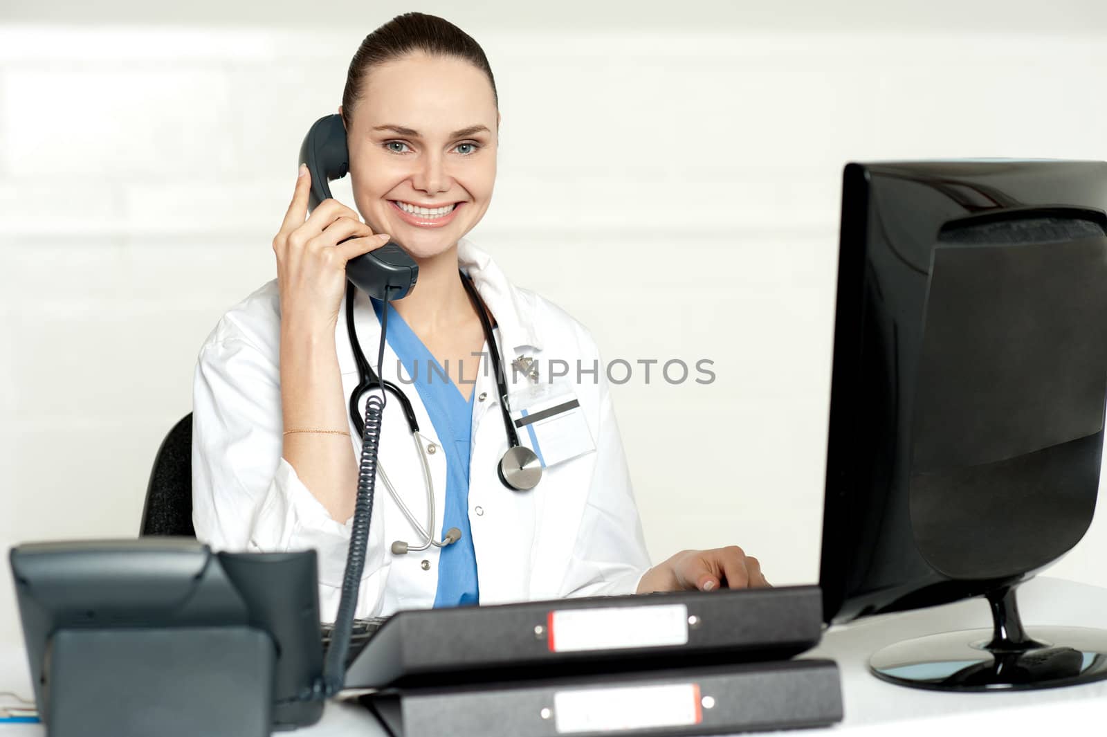 Young smiling physician sitting in clinic and communicating on phone