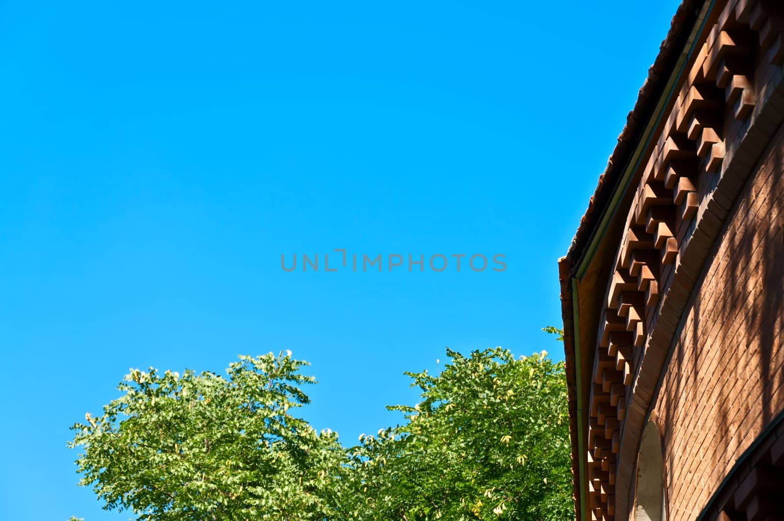 Fragment of a circular brick wall against the blue sky and green trees.