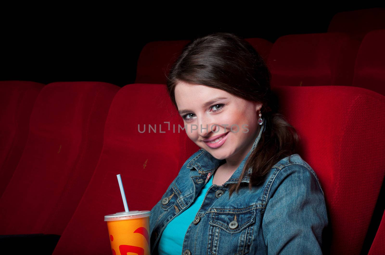 portrait of a beautiful woman in a movie theater, holding a glass of drink