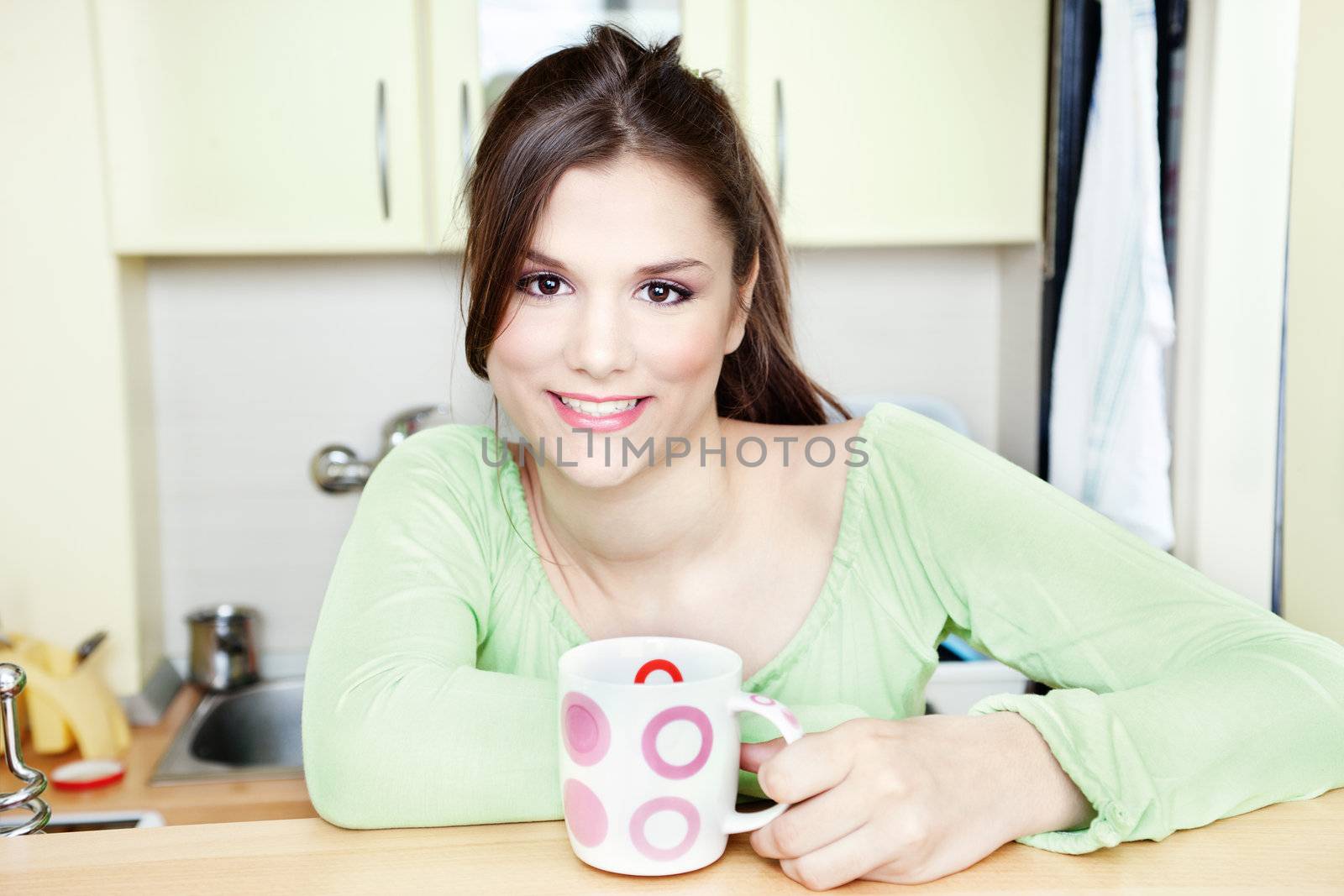 Happy girl holding big cup of tea in kitchen