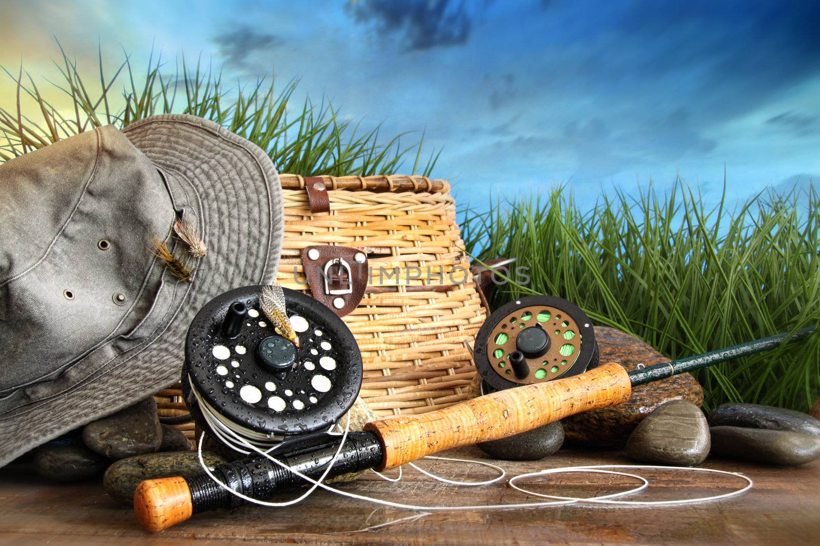 Fly fishing equipment with hat on wooden dock by Sandralise