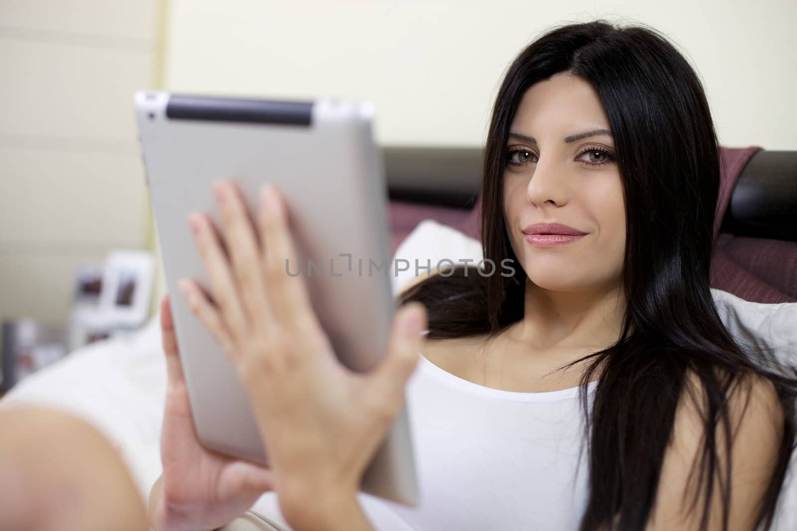 Beautiful woman in bed with tablet smiling by fmarsicano