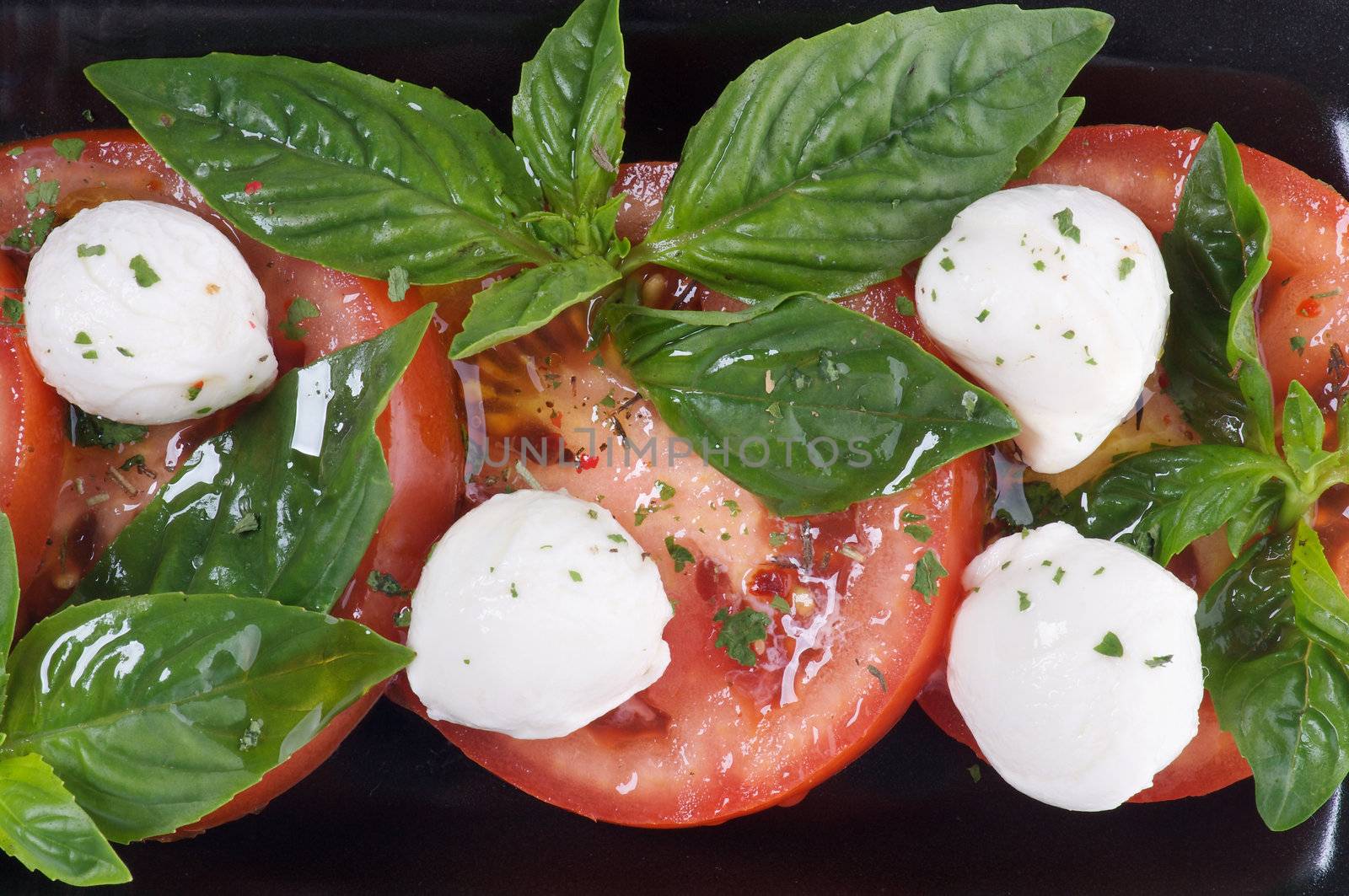Italian Caprese Salad with Basil, Fresh Mozzarella, Tomatoes and Olive Oil on black plate close up