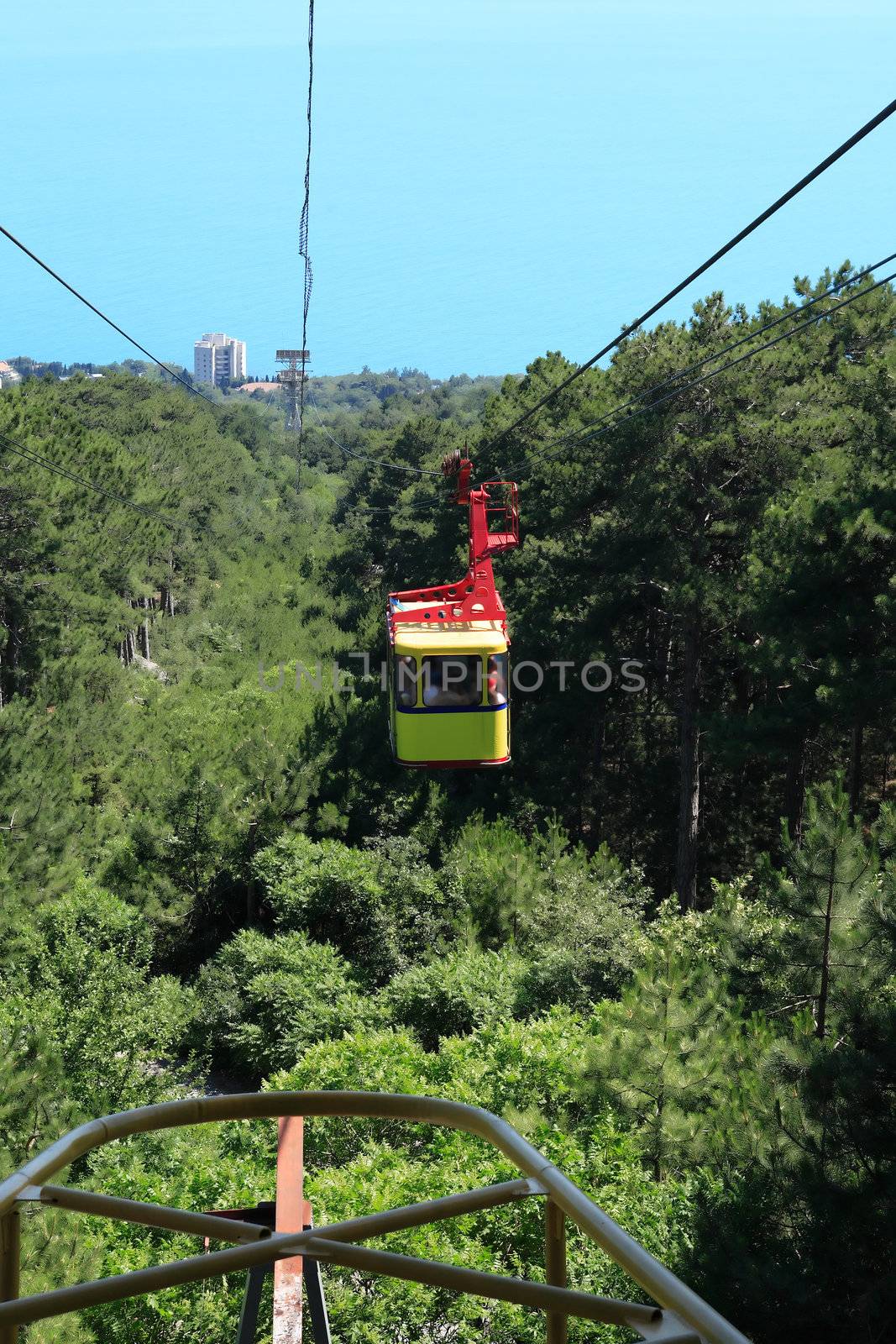 Yellow overhead cable car moving from mountain to sea above forest