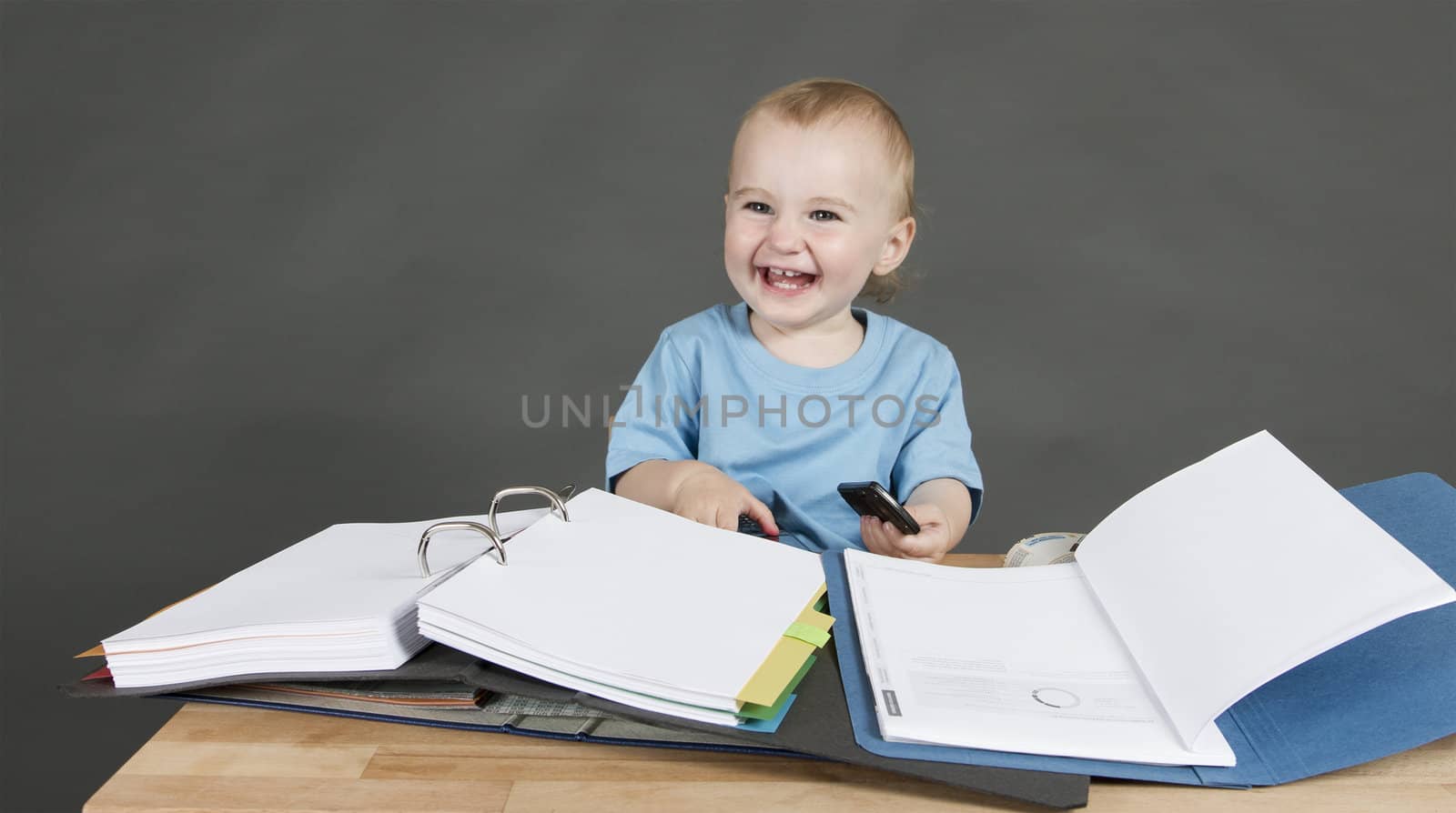 laughing child with paperwork at desk in grey background