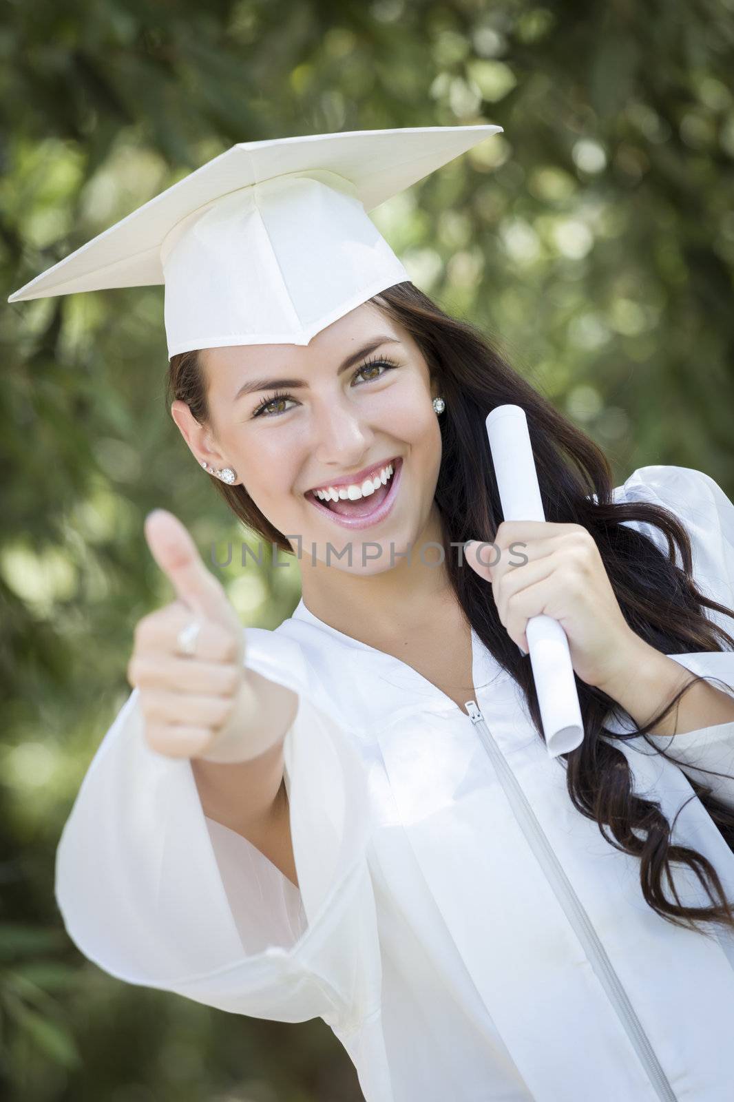 Attractive Mixed Race Girl Celebrating Graduation Outside In Cap and Gown with Diploma in Hand.