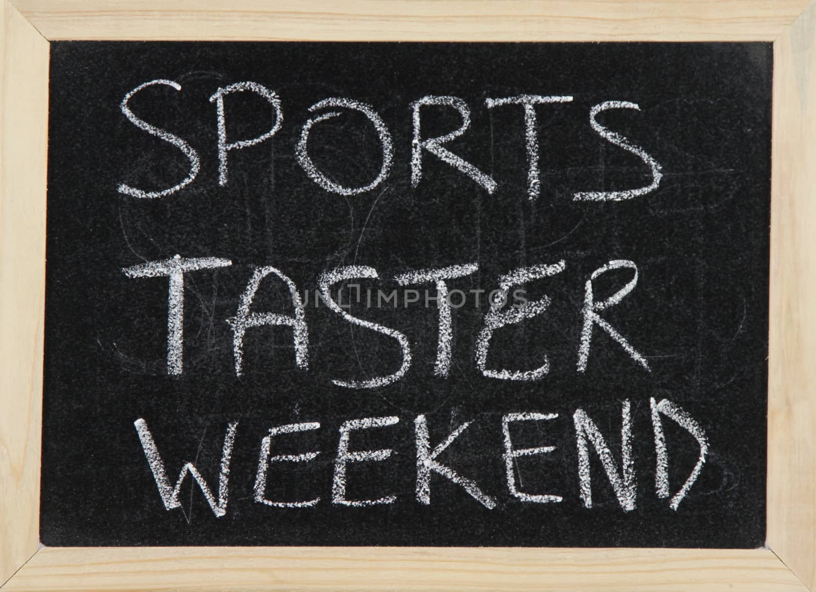 A blackboard with a wooden border with the words 'SPORTS TASTER WEEKEND' written by hand in white chalk.