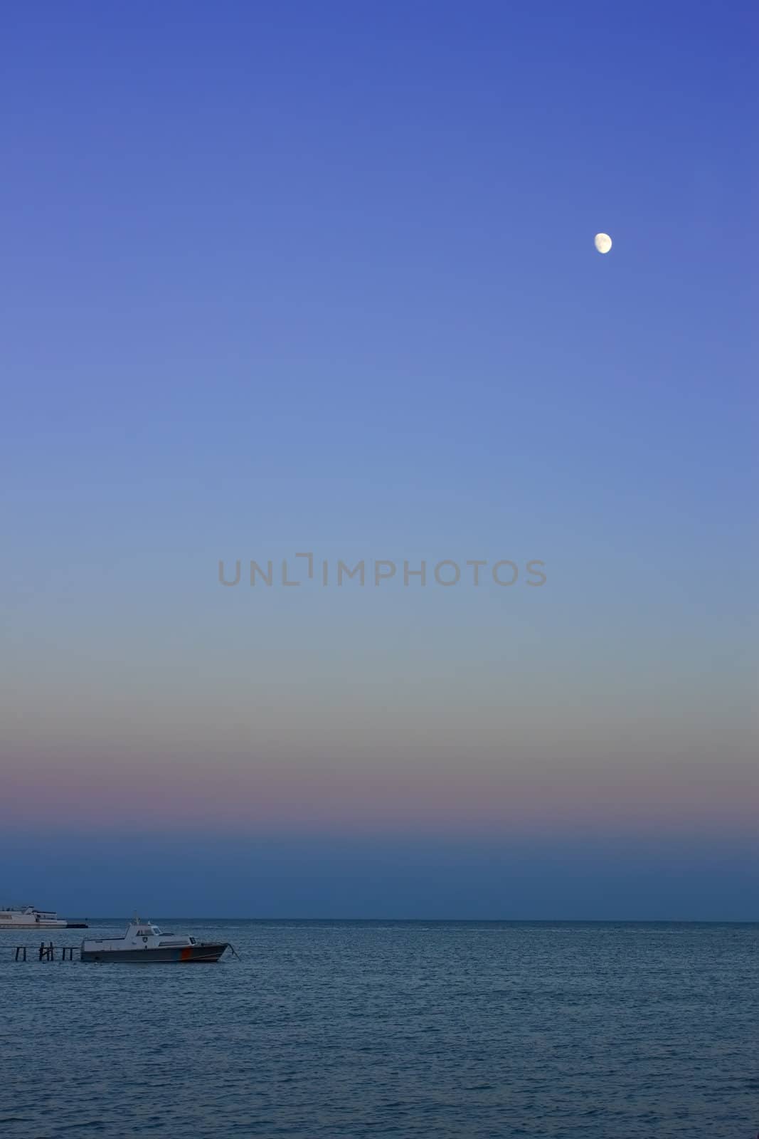 Night at sea. The moon in the cloudless sky illuminating motor boats near a pier