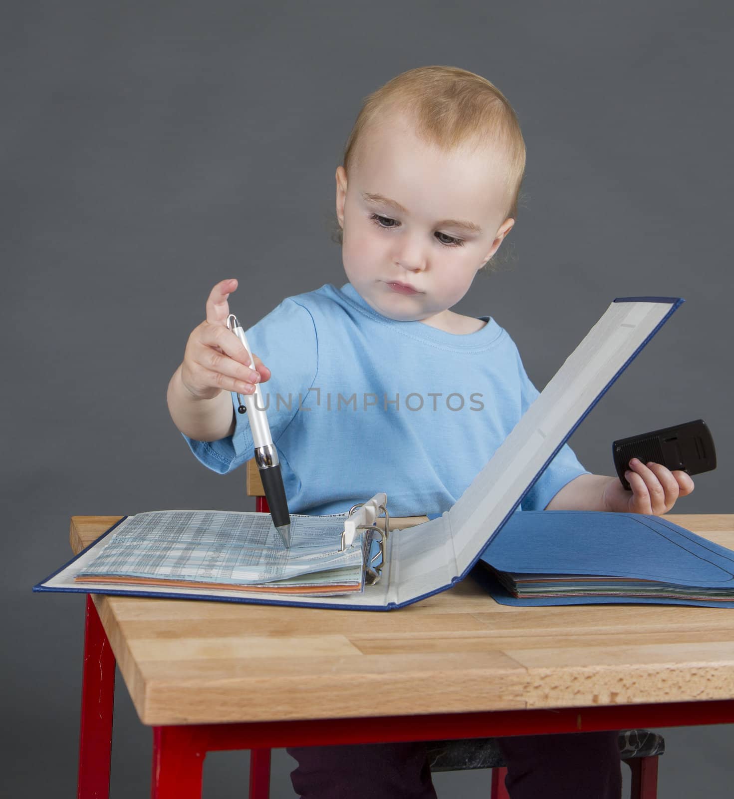 baby with paperwork at wooden desk in grey background