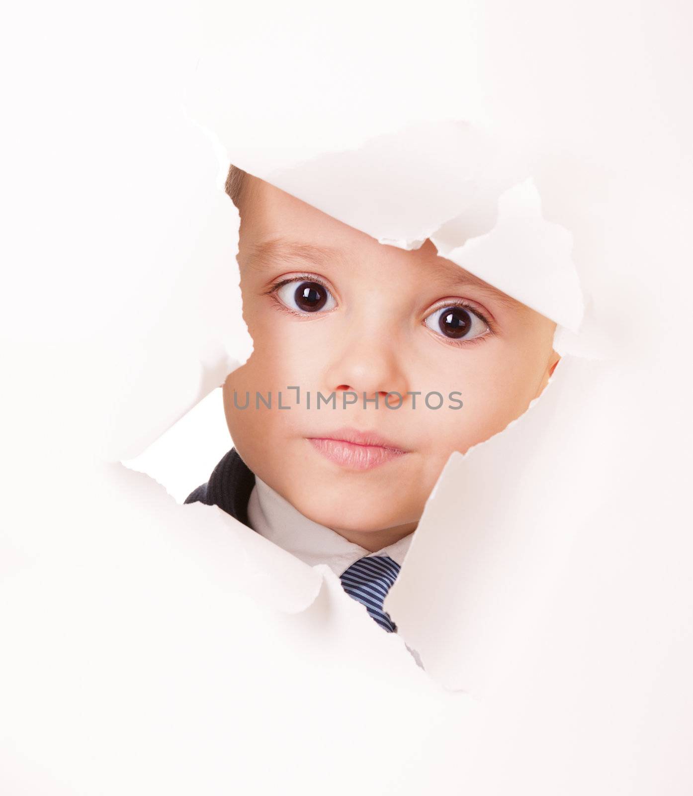Serious kid looks through a hole in white paper