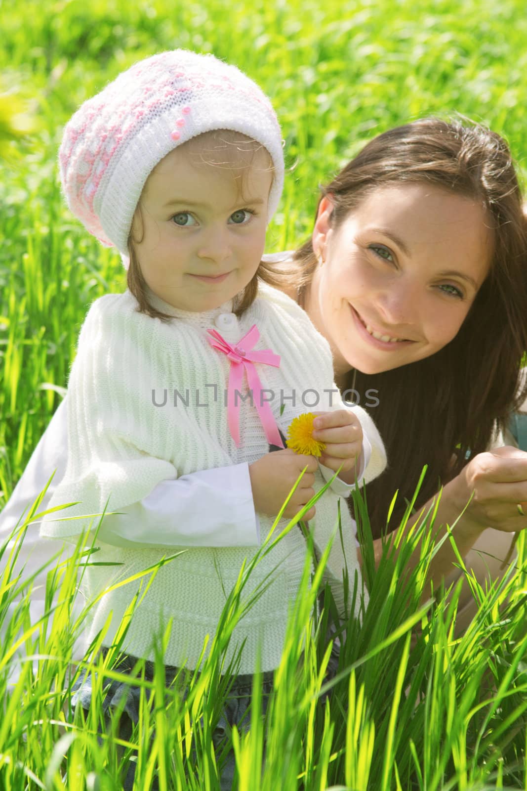 Smiling mother and daughter among green grass