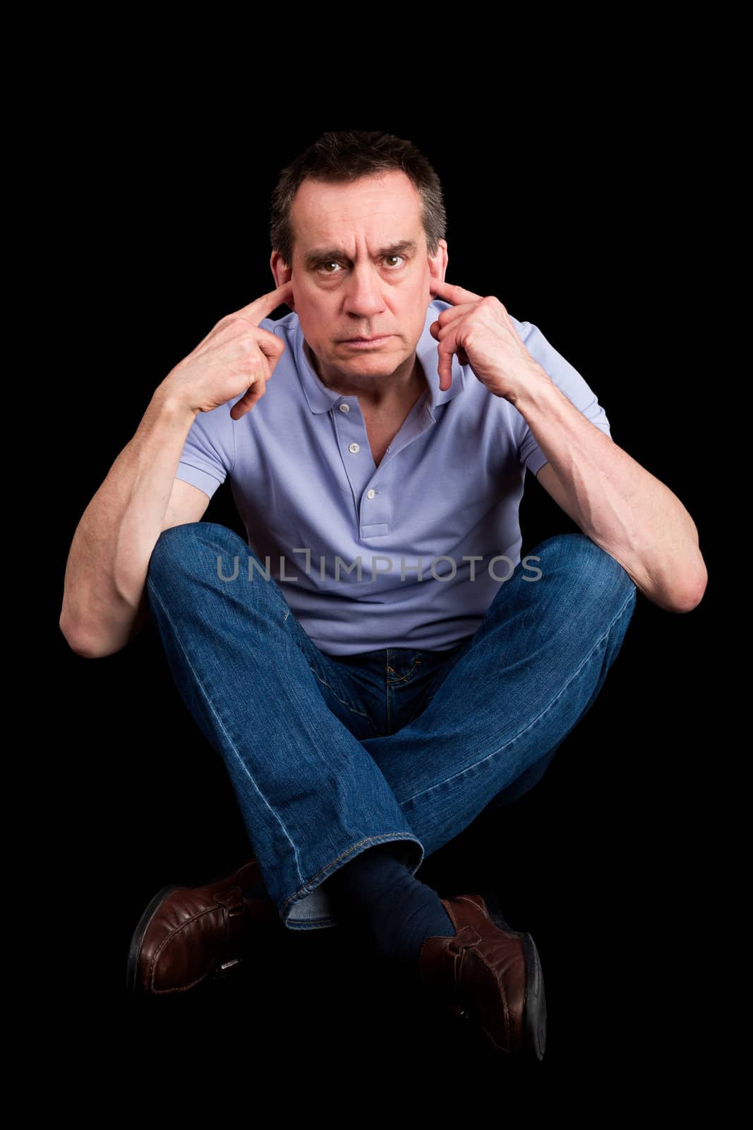 Angry Frowning Middle Age Man Fingers in Ears Not Listening Cross Legged Black Background