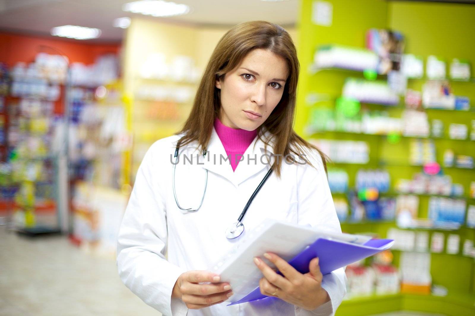 Serious female doctor in pharmacy with documents in her hand by fmarsicano