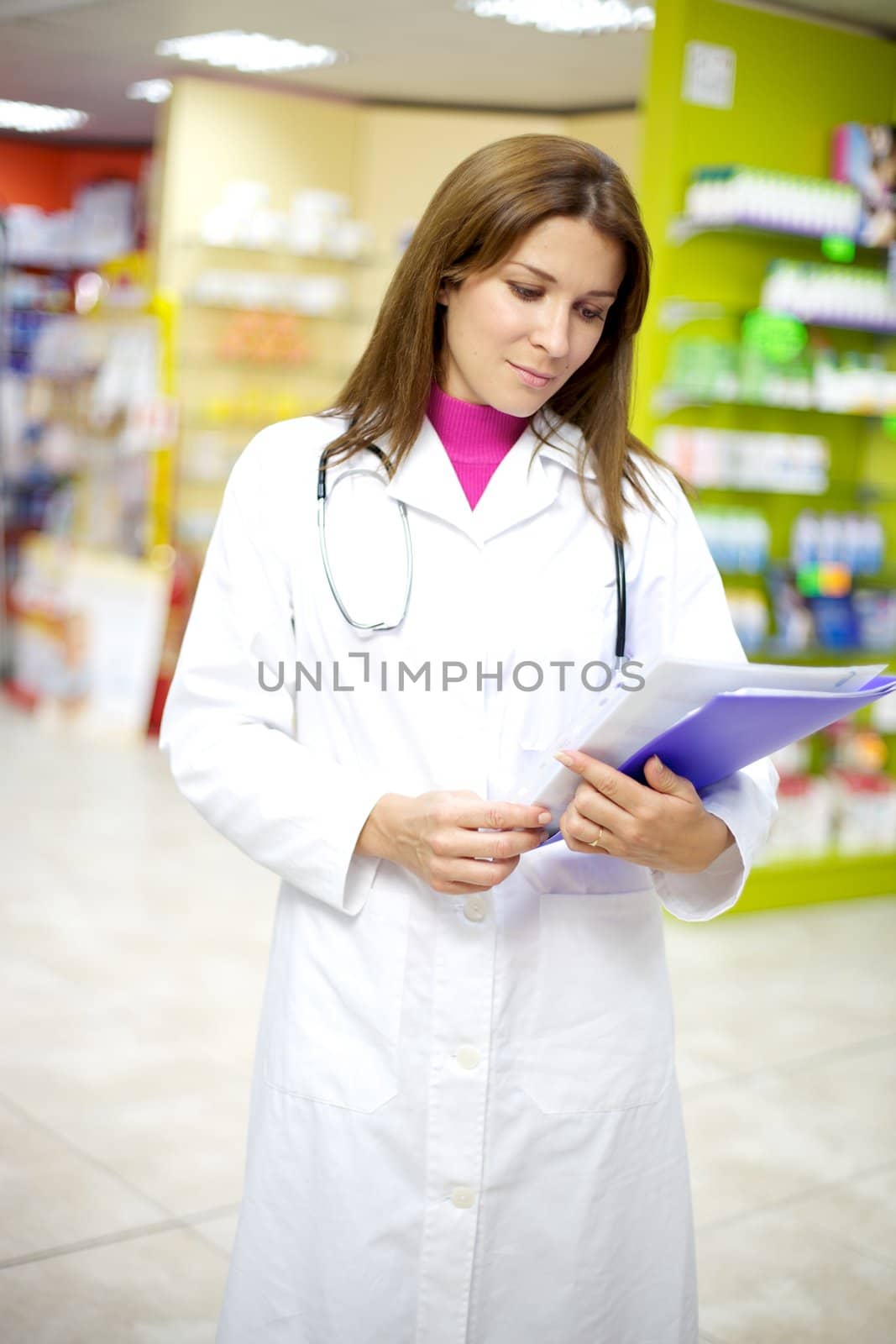 Serious female doctor watching documents inside pharmacy by fmarsicano