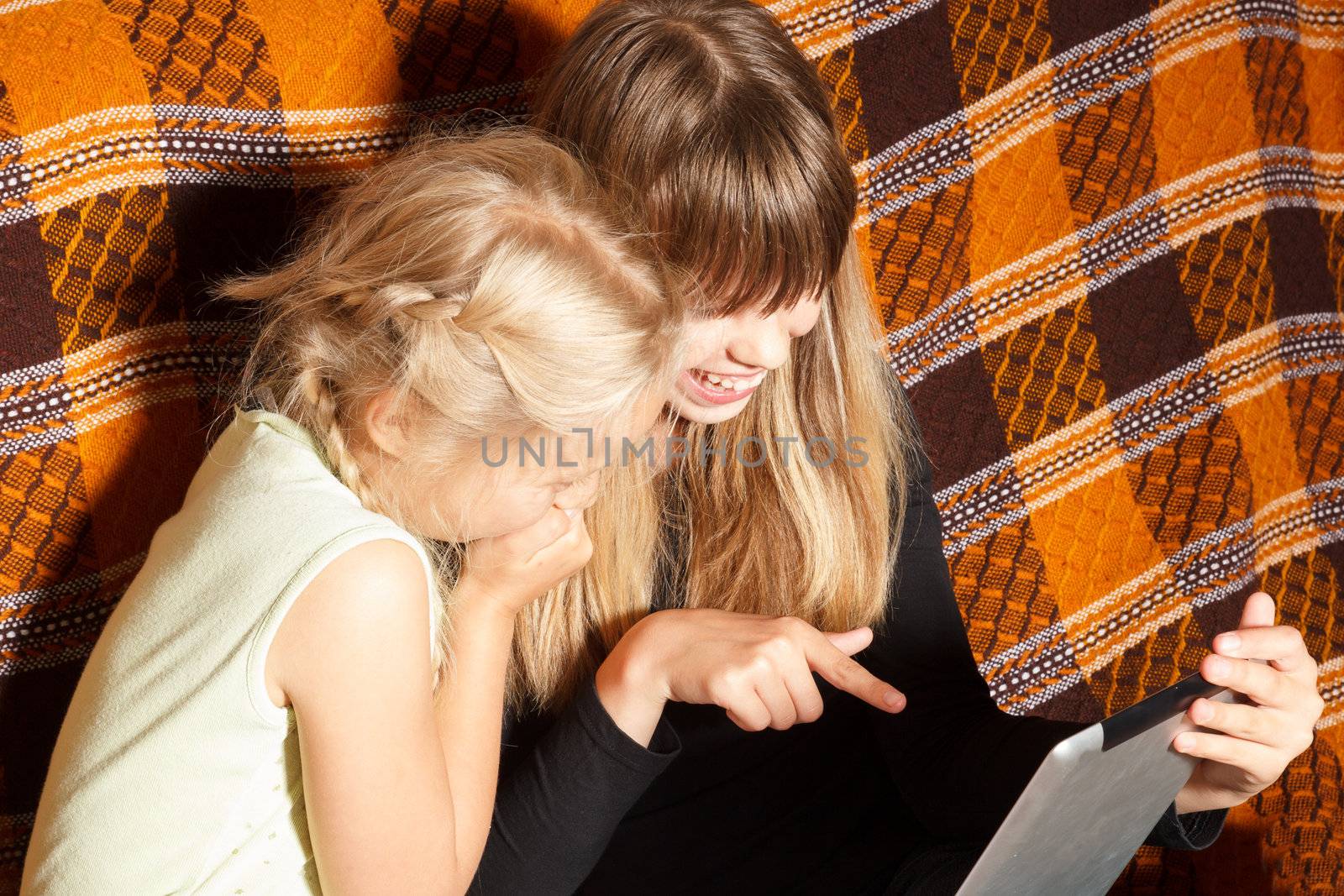 two sisters laughing while watching movies on a tablet